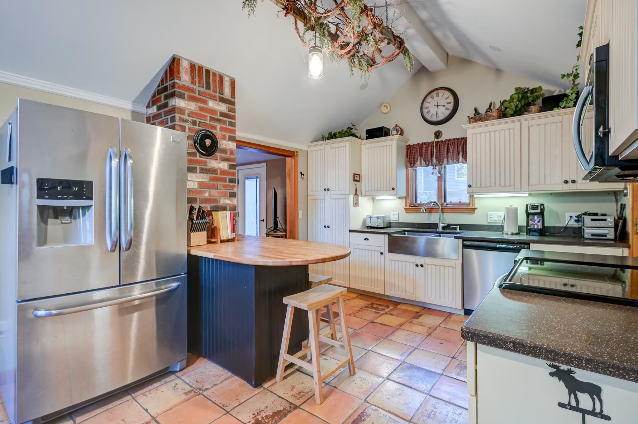 Kitchen with white cabinets, stainless steel appliances, a wood-topped island, and terracotta tile floor.