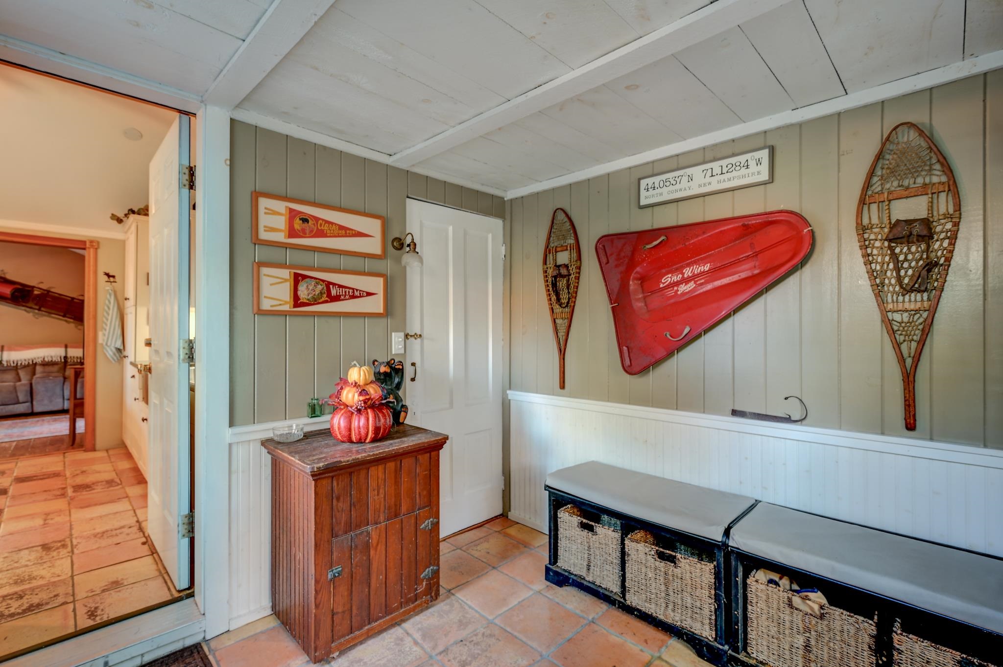 Entry room with terracotta tile, built-in storage bench, red sled, and snowshoes on the wall.