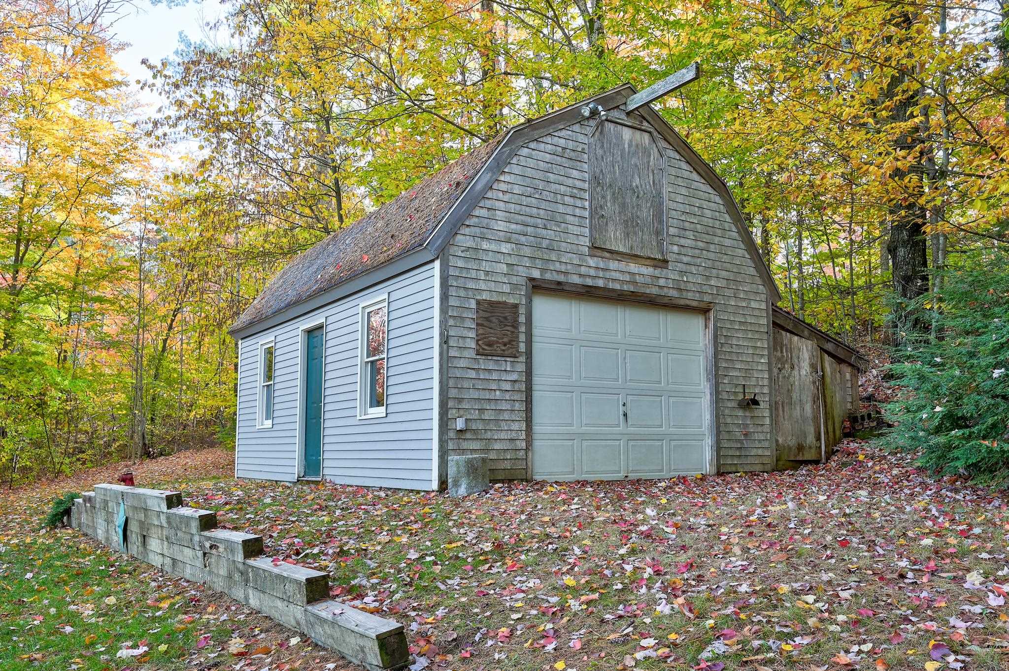 Barn-style garage with a large white door, framed by colorful autumn trees.