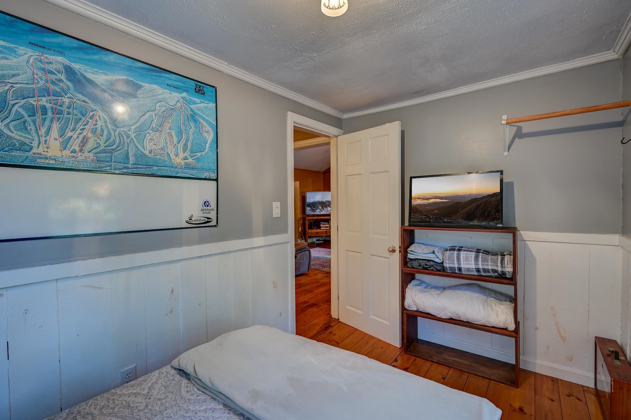 Bedroom with an Attitash ski trail map, wood floors, and bedding on open shelves.