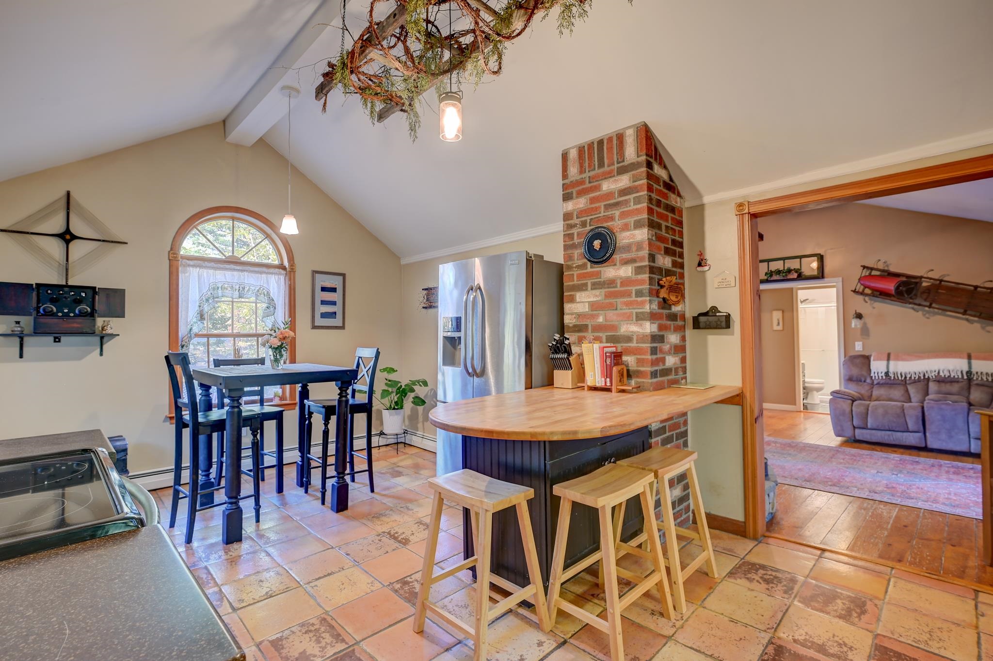 Kitchen with a wood-topped island, brick chimney, terracotta floors, and arched dining-area window.