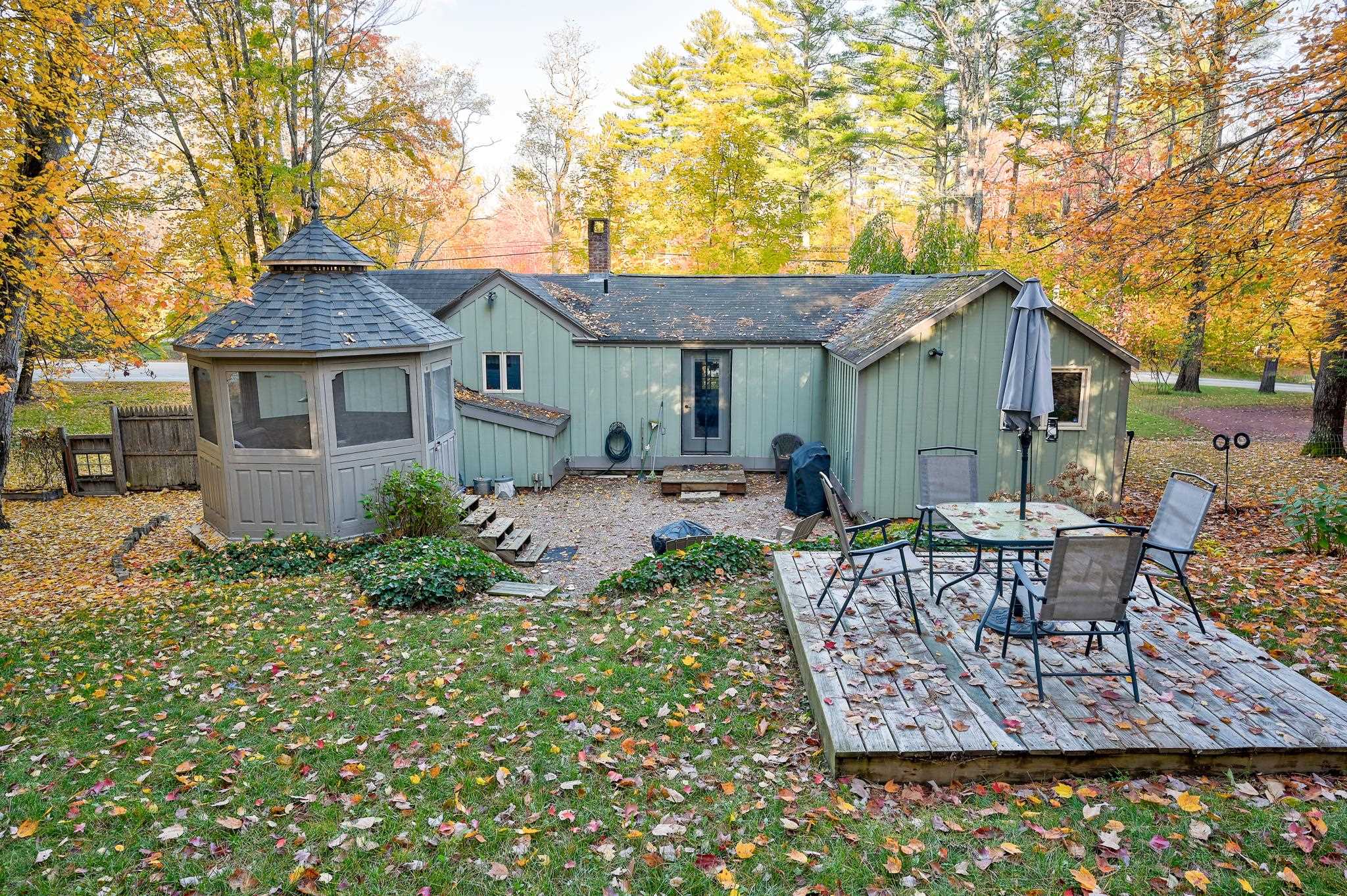 Home’s rear exterior with a screened gazebo and furnished deck amid autumn foliage.