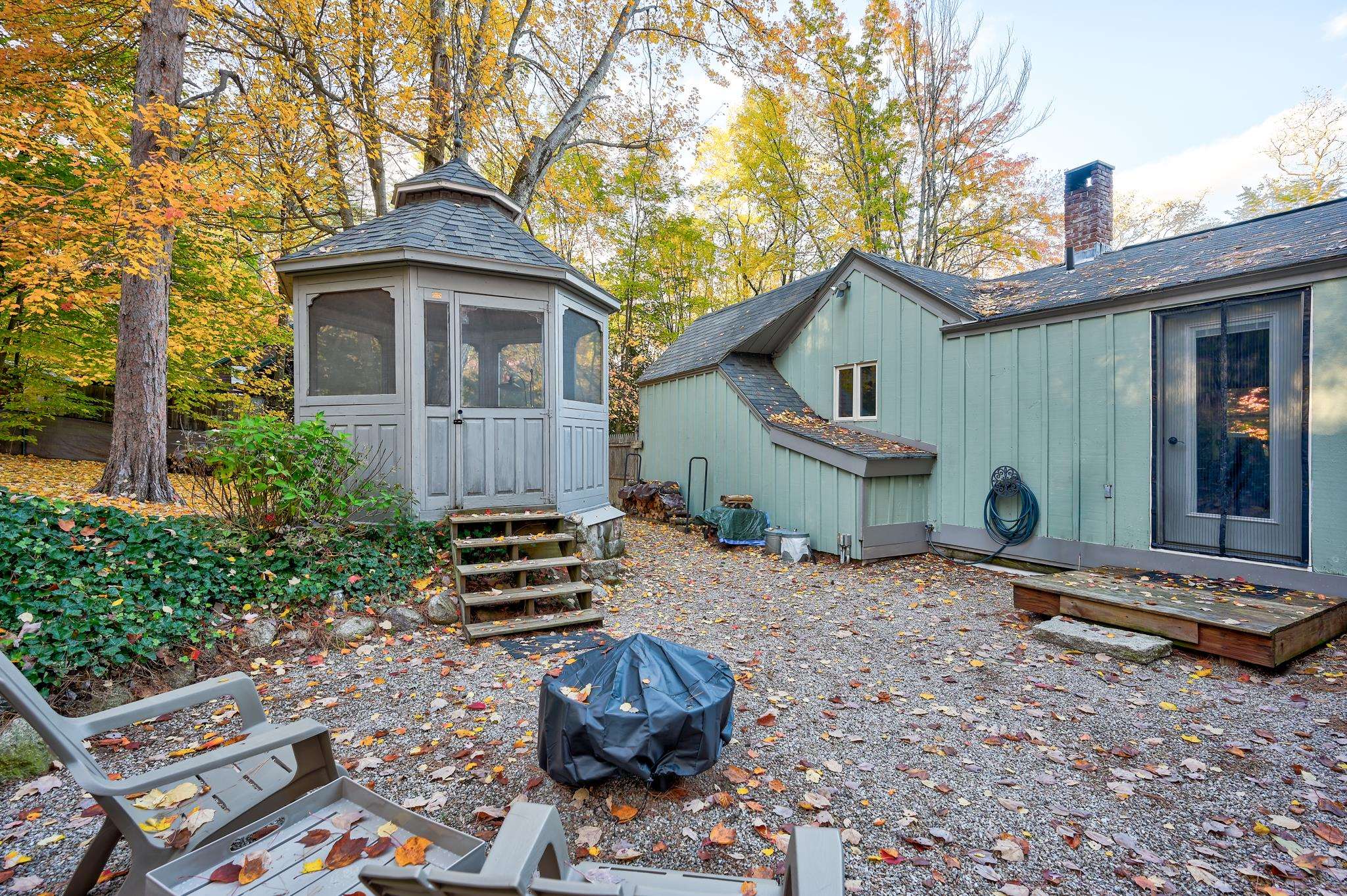 Gravel patio beside a pale green house, with a screened gazebo and autumn foliage.