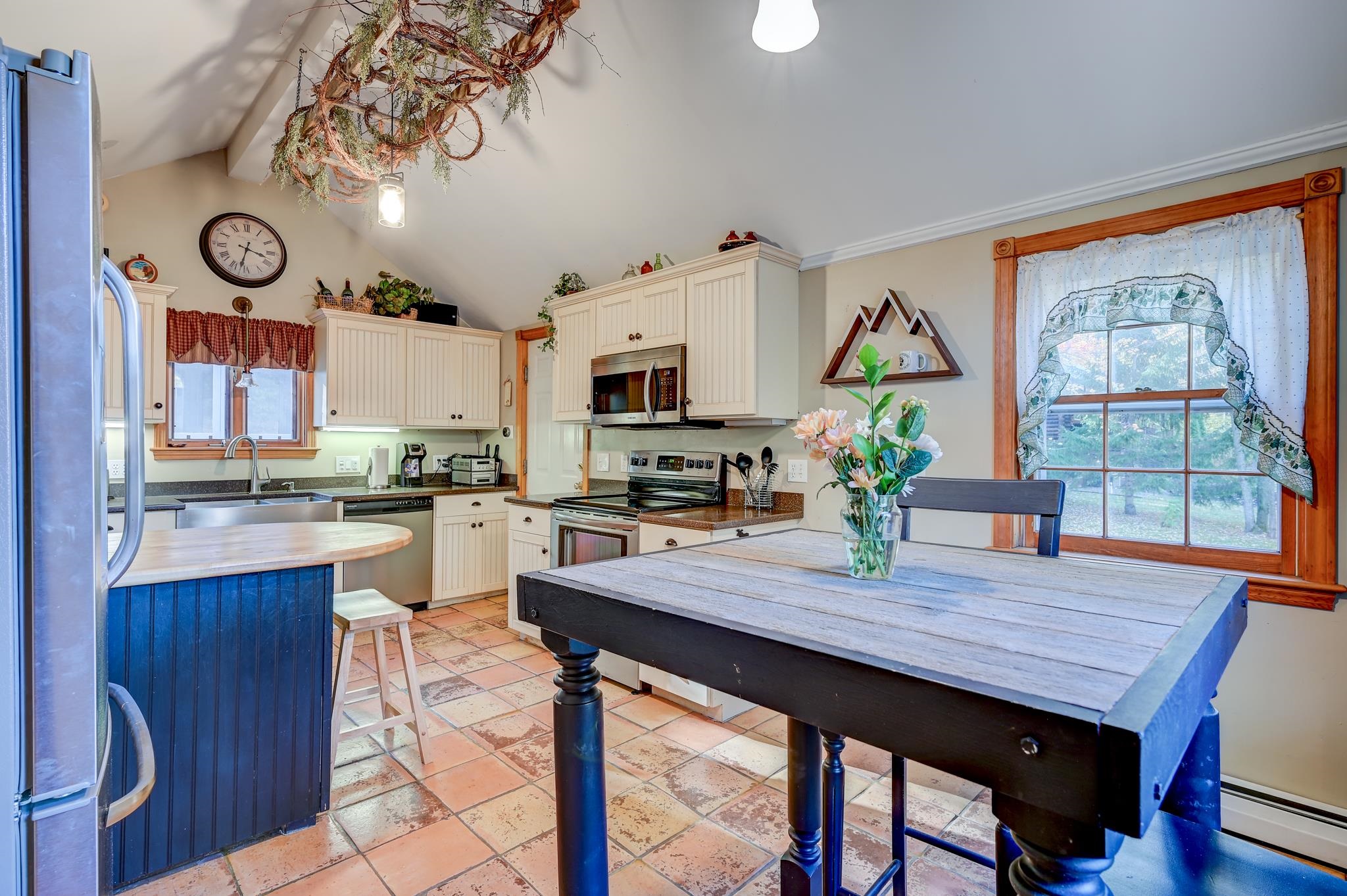 Kitchen with cream cabinets, terracotta tile, a blue island, and a large dining table by the window.