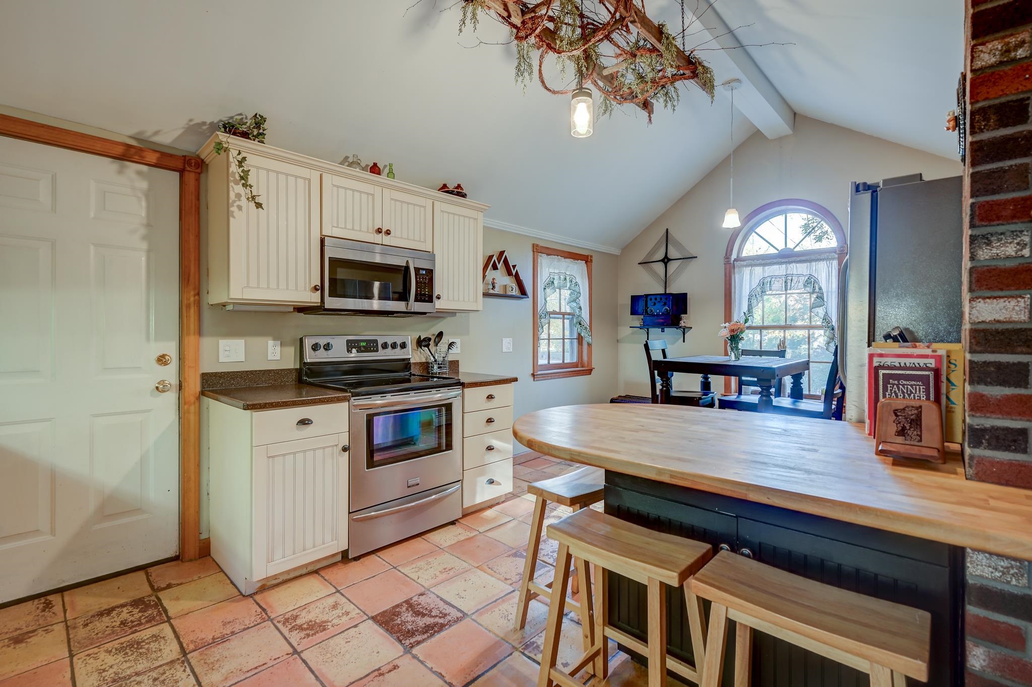 Kitchen with cream cabinets, terracotta tile floors, and a butcher-block island with stools.