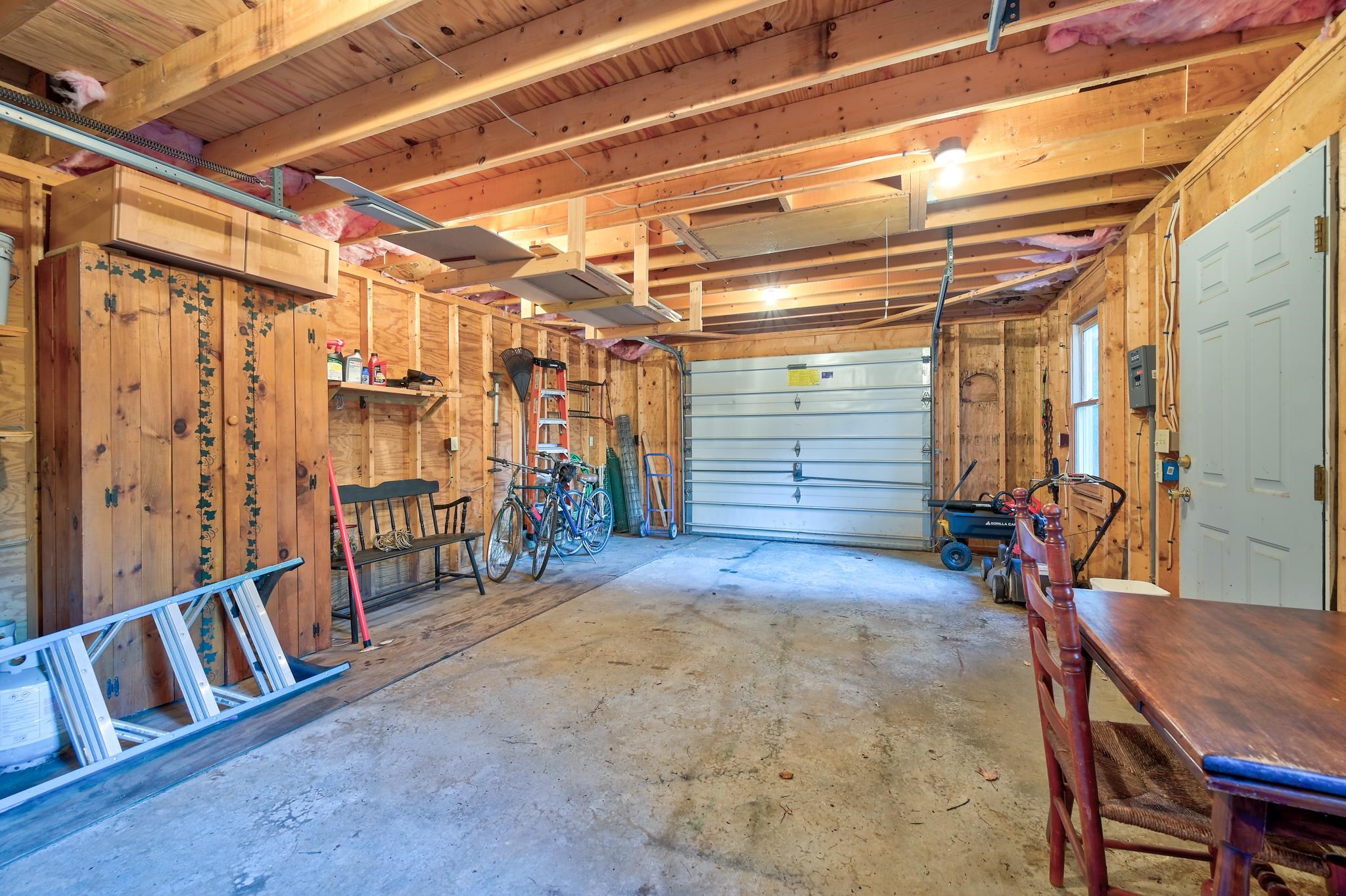 Garage with exposed wood framing, a concrete floor, bicycles, and a closed sectional door.