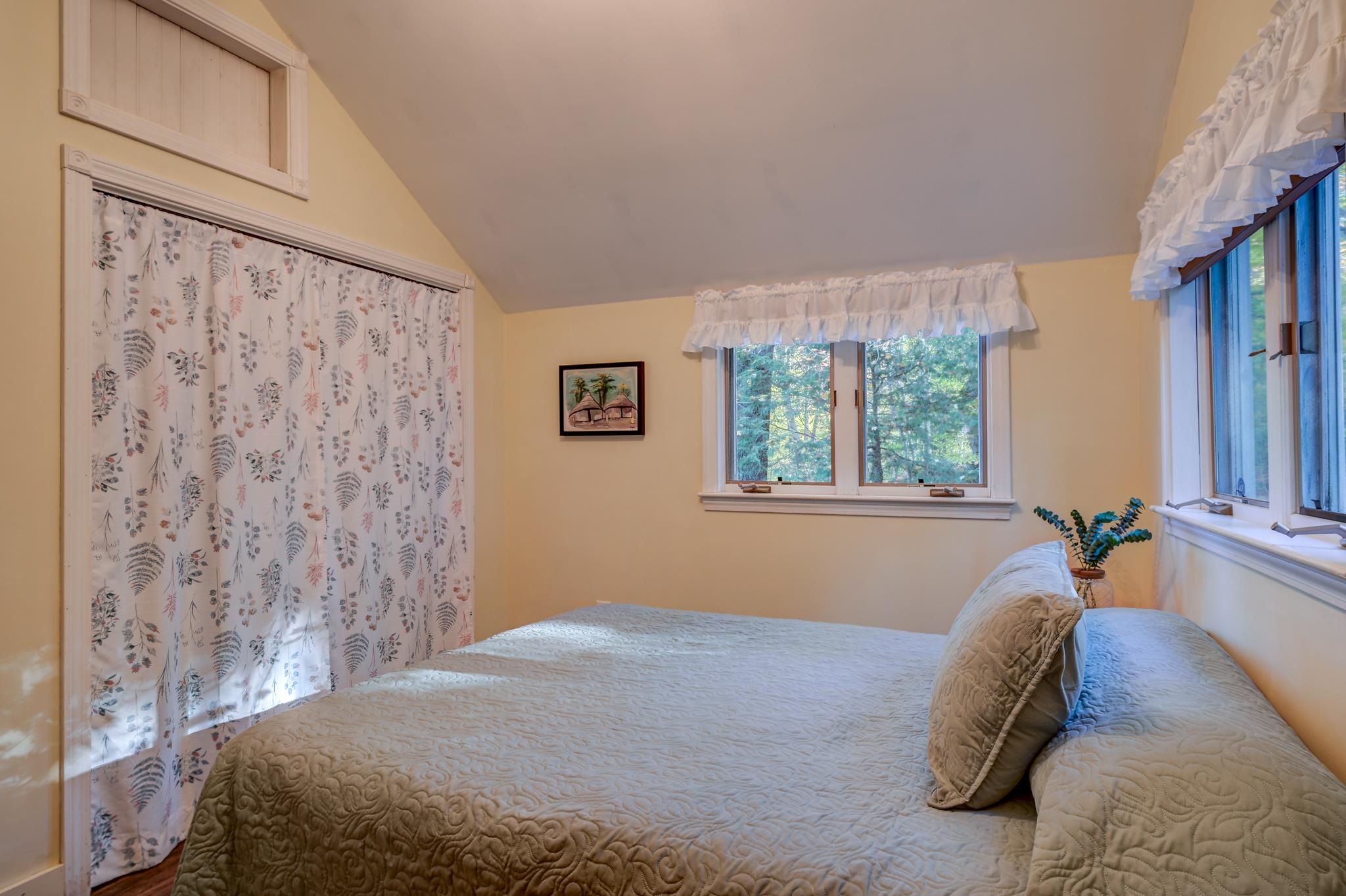 Bedroom with a quilt-covered bed and windows overlooking trees.