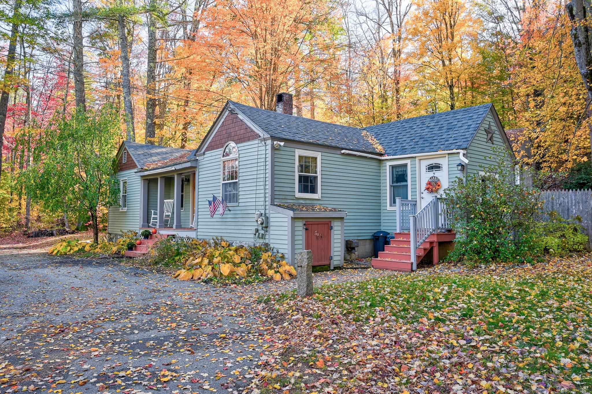 Light blue-green house with a covered porch and red steps amid autumn foliage.
