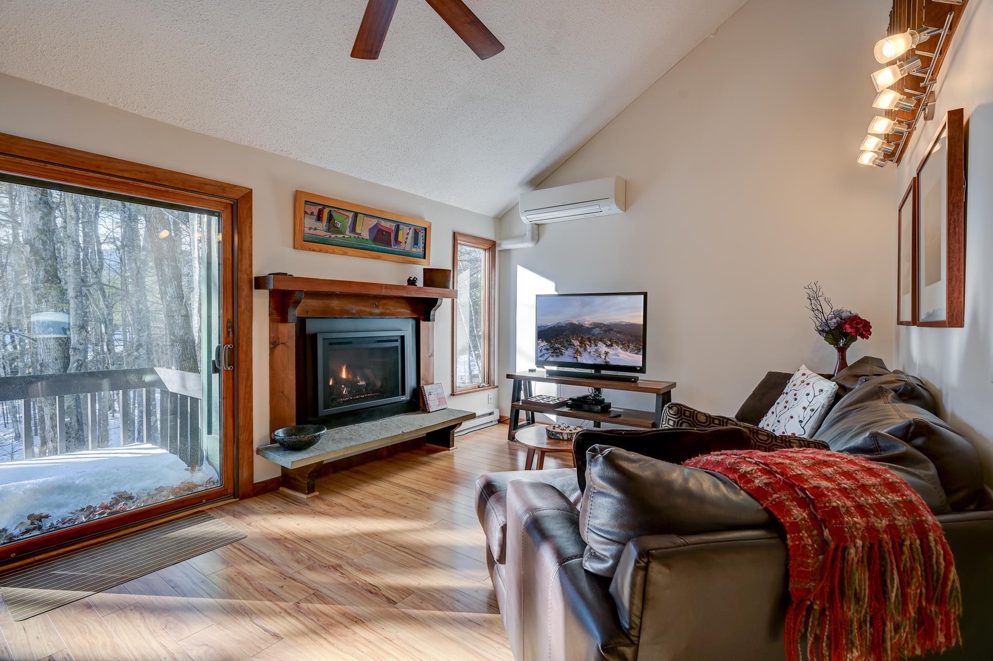 Living room with a wood-trimmed fireplace, leather sectional, and sliding doors overlooking snowy woods.