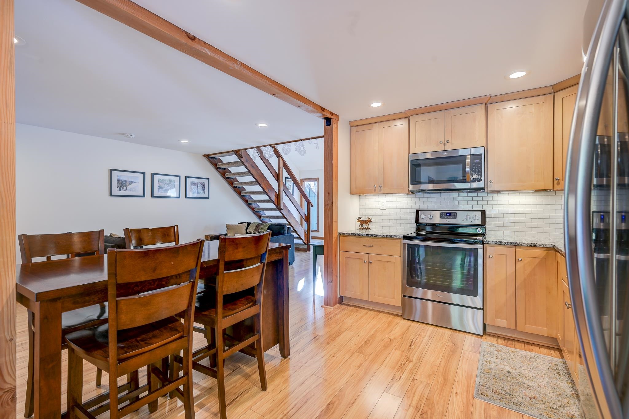 Open kitchen and dining area with light wood cabinets, stainless steel appliances, and an open staircase.