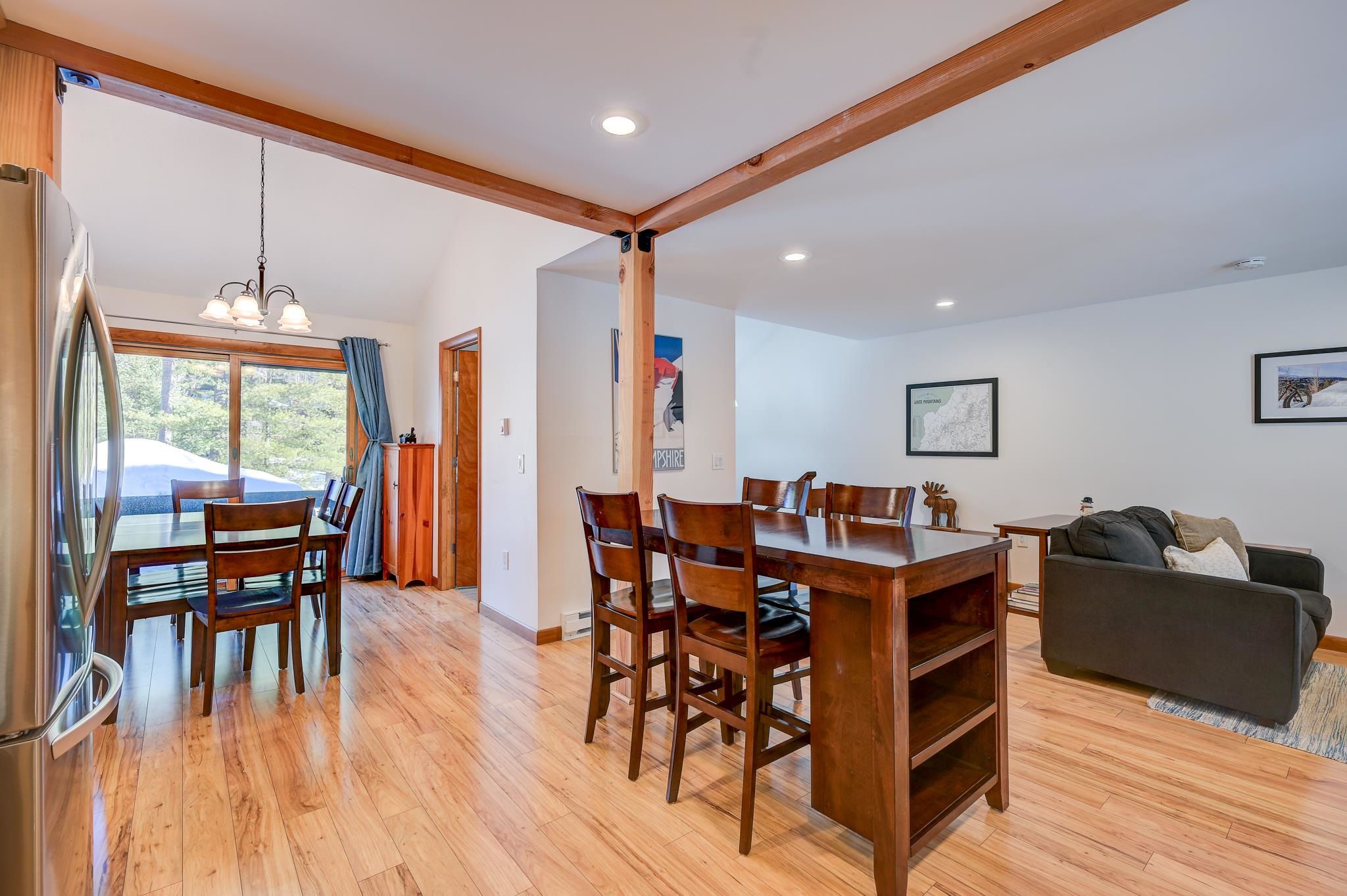 Open-plan dining and living area with timber ceiling beams, wooden tables, and a sliding glass door.