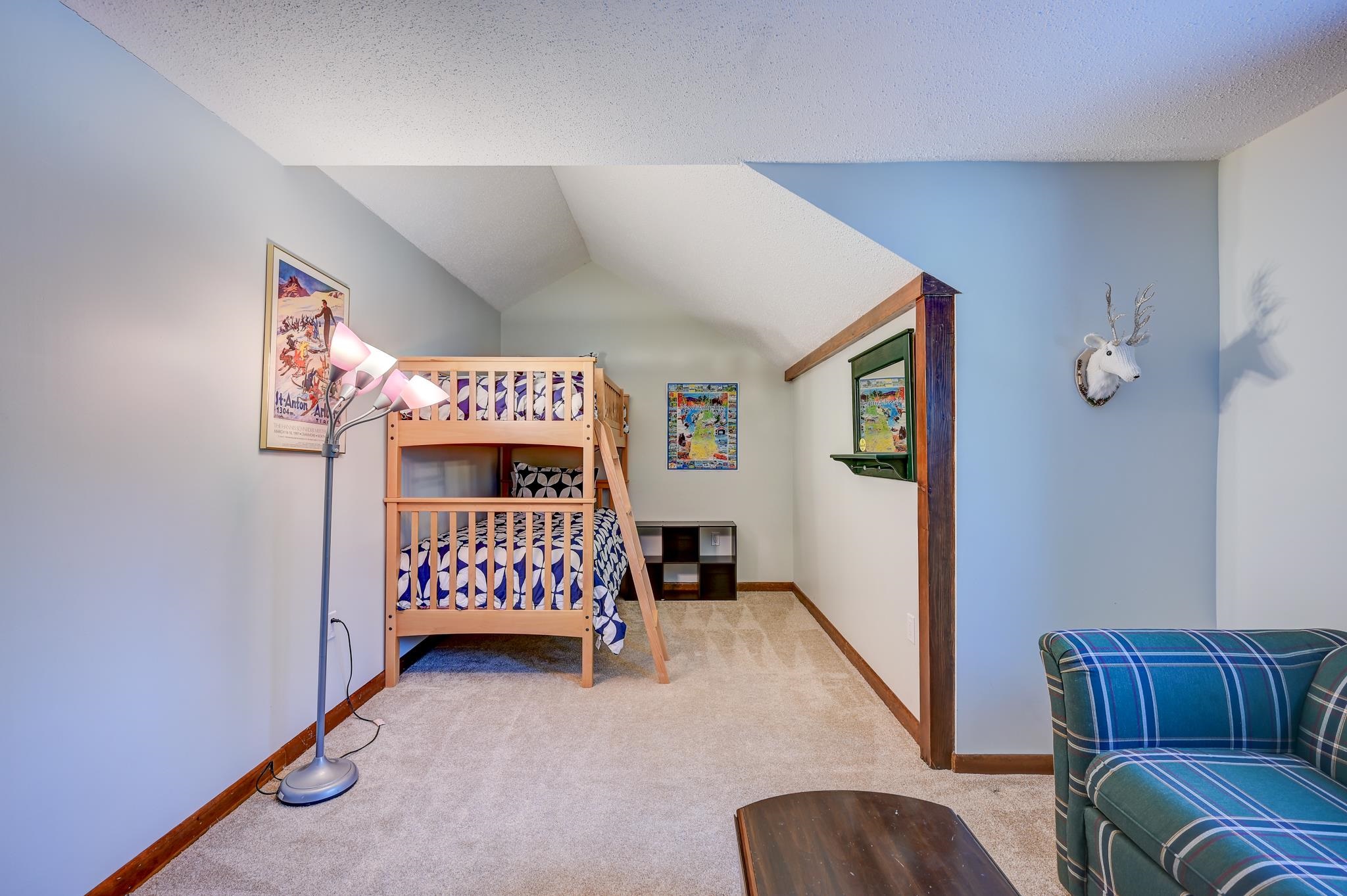 Loft bedroom with a wooden bunk bed beneath a sloped ceiling and a blue plaid armchair.