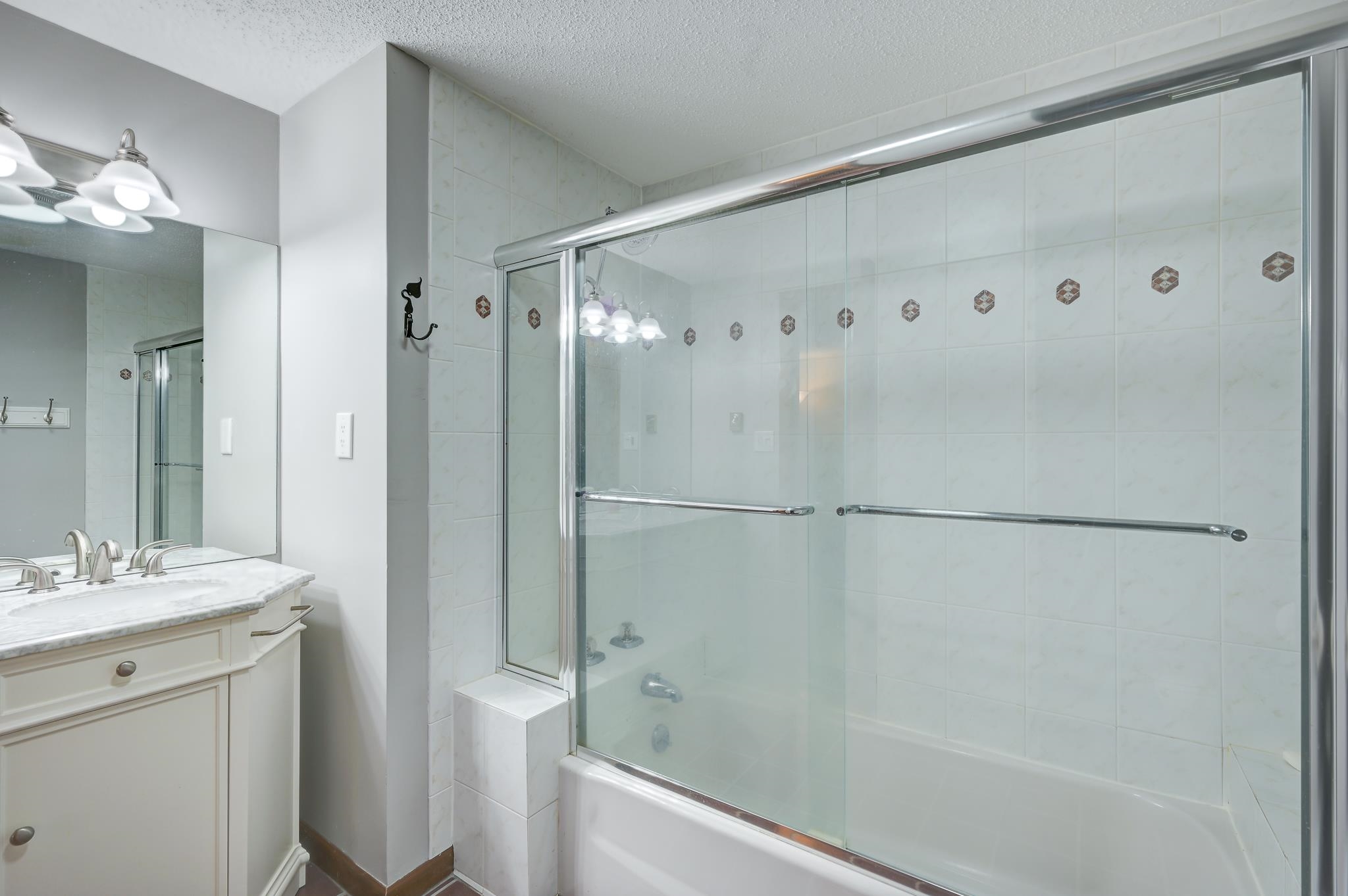 Bathroom with a white vanity beside a bathtub with clear sliding glass doors.
