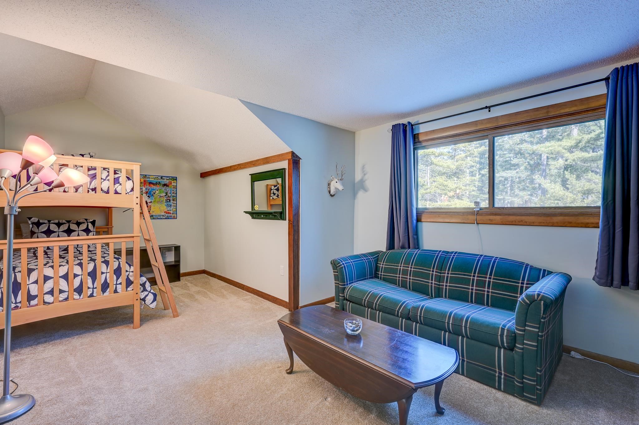 Bedroom with a wooden bunk bed, plaid sofa, and large window overlooking trees.