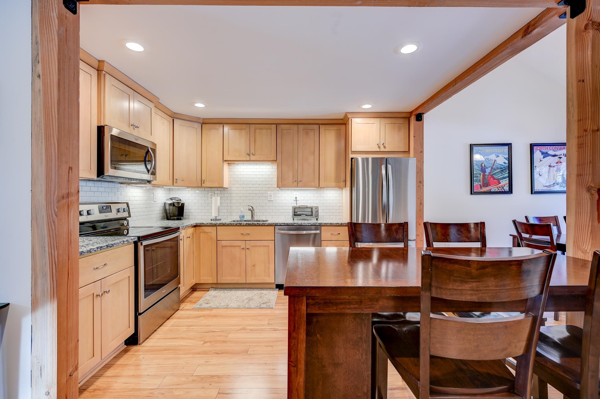 Kitchen and dining area with light wood cabinetry, stainless steel appliances, and a dark wood table.