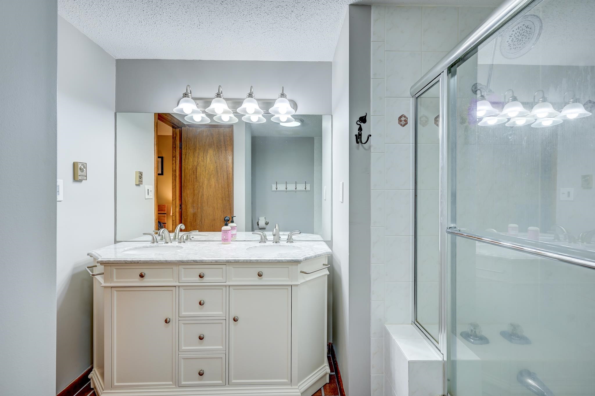 Bathroom with a white vanity, large mirror, and glass-enclosed shower.