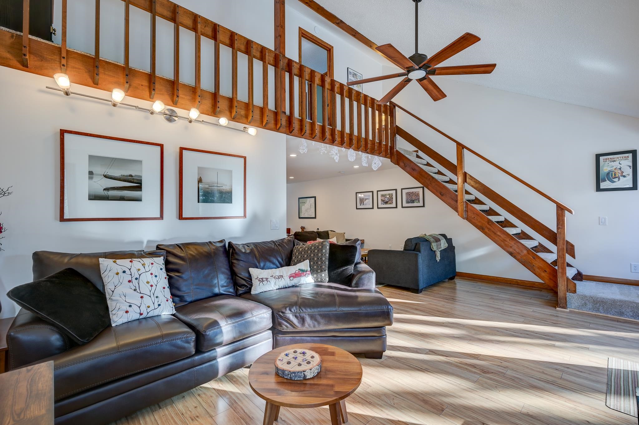 Living room with a dark leather sectional and an open wooden staircase to a loft.