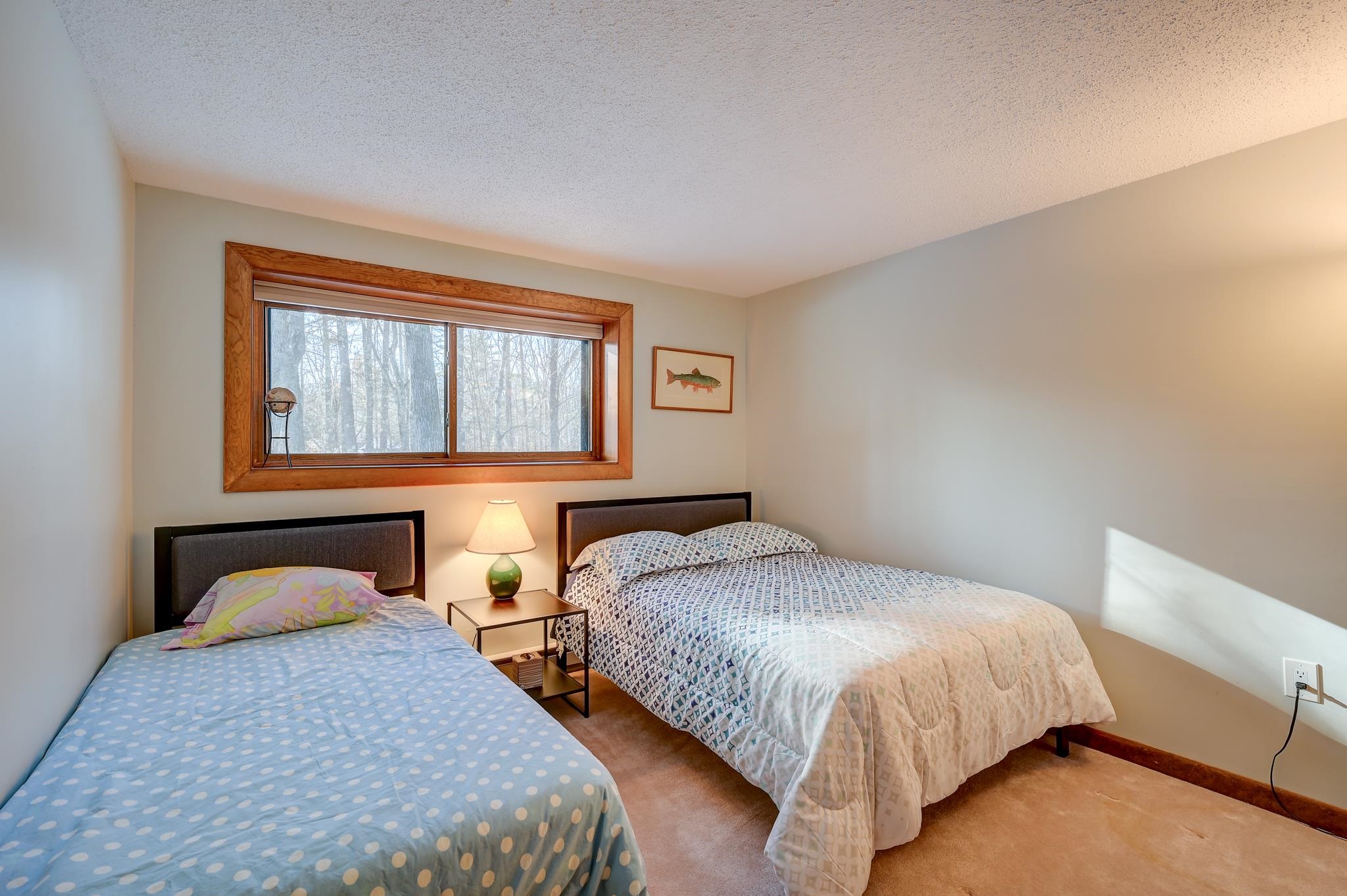 Bedroom with two beds and a wide wood-trimmed window overlooking leafless trees.