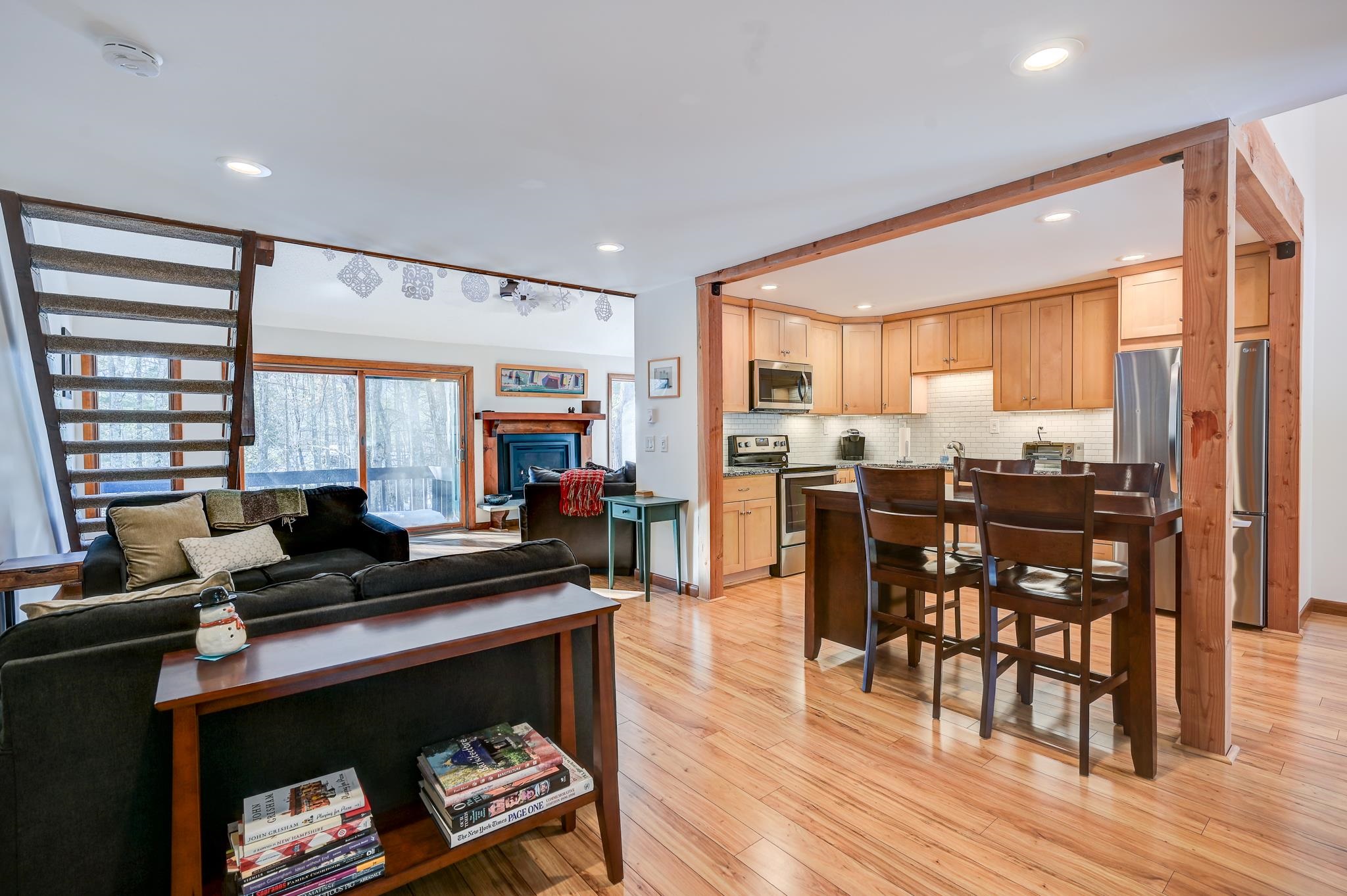 Open-plan condo living room and kitchen with a fireplace, timber framing, and wooded views through sliding doors.