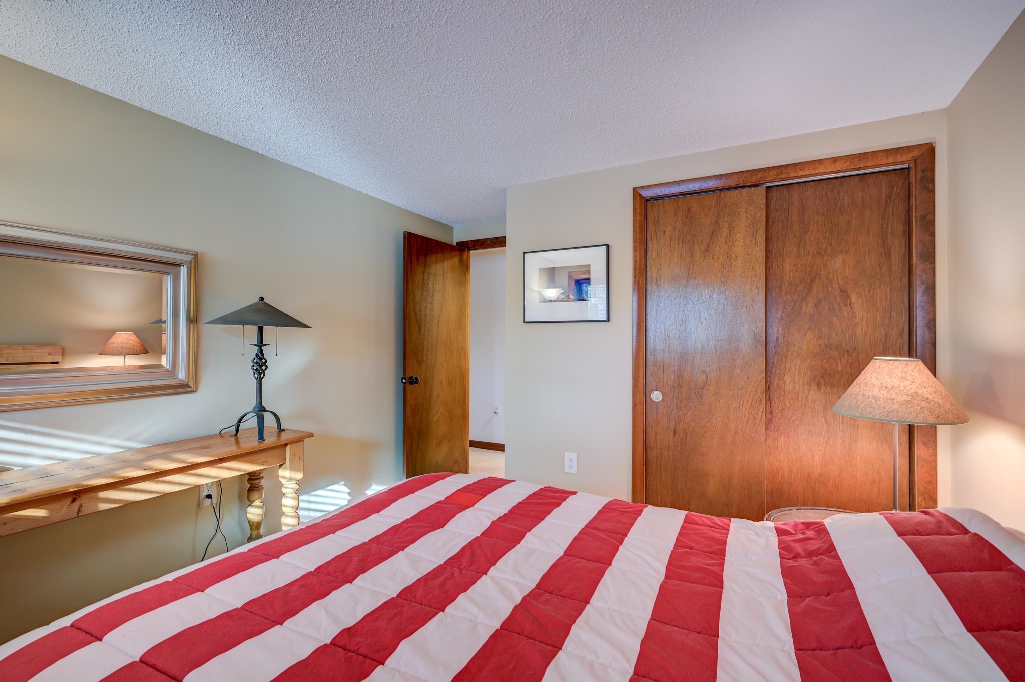 Bedroom with a red-and-white striped quilt, wooden closet doors, and a desk beneath a large mirror.