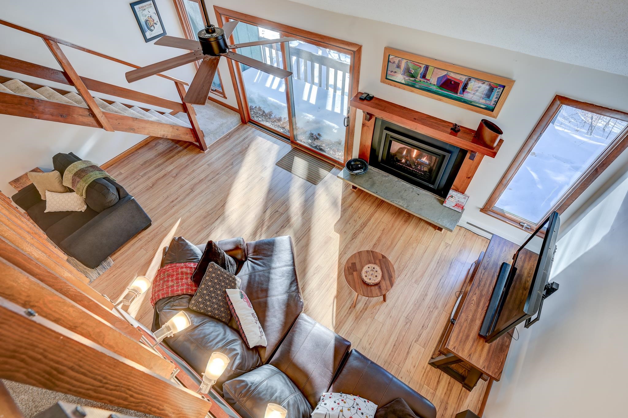 Living room with exposed wood beams, leather sofas, a fireplace, and snowy views through large windows.