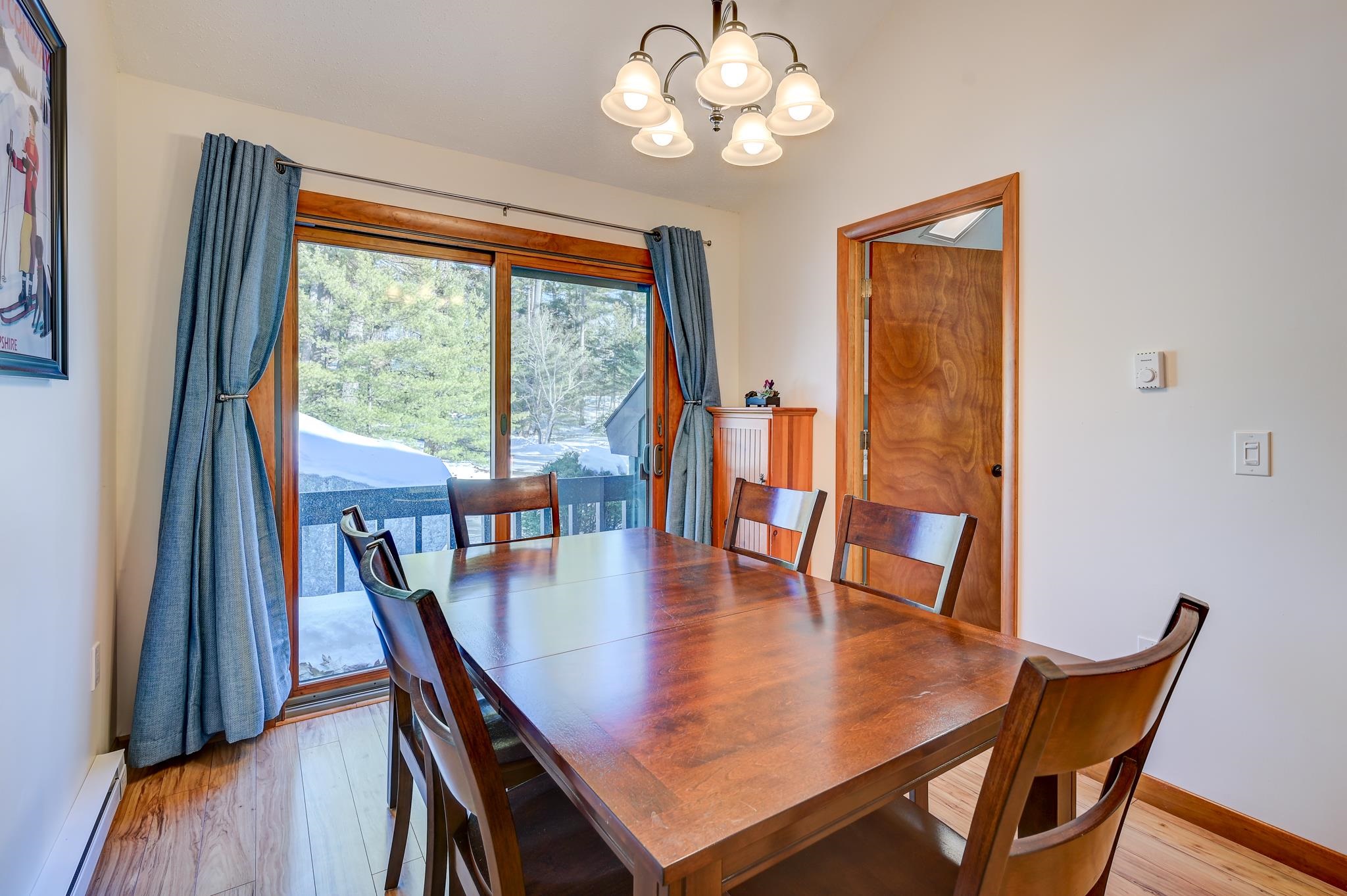 Dining room with a wooden table and chairs beside a sliding glass door overlooking snowy trees.