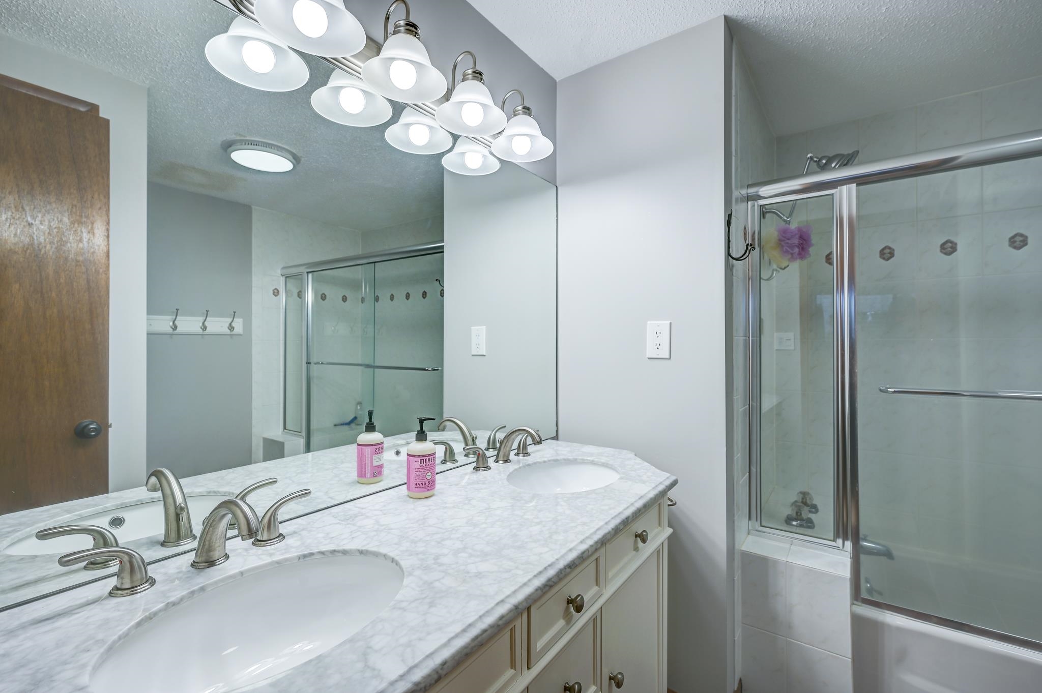 Bathroom with a double-sink vanity and glass-enclosed tub and shower.