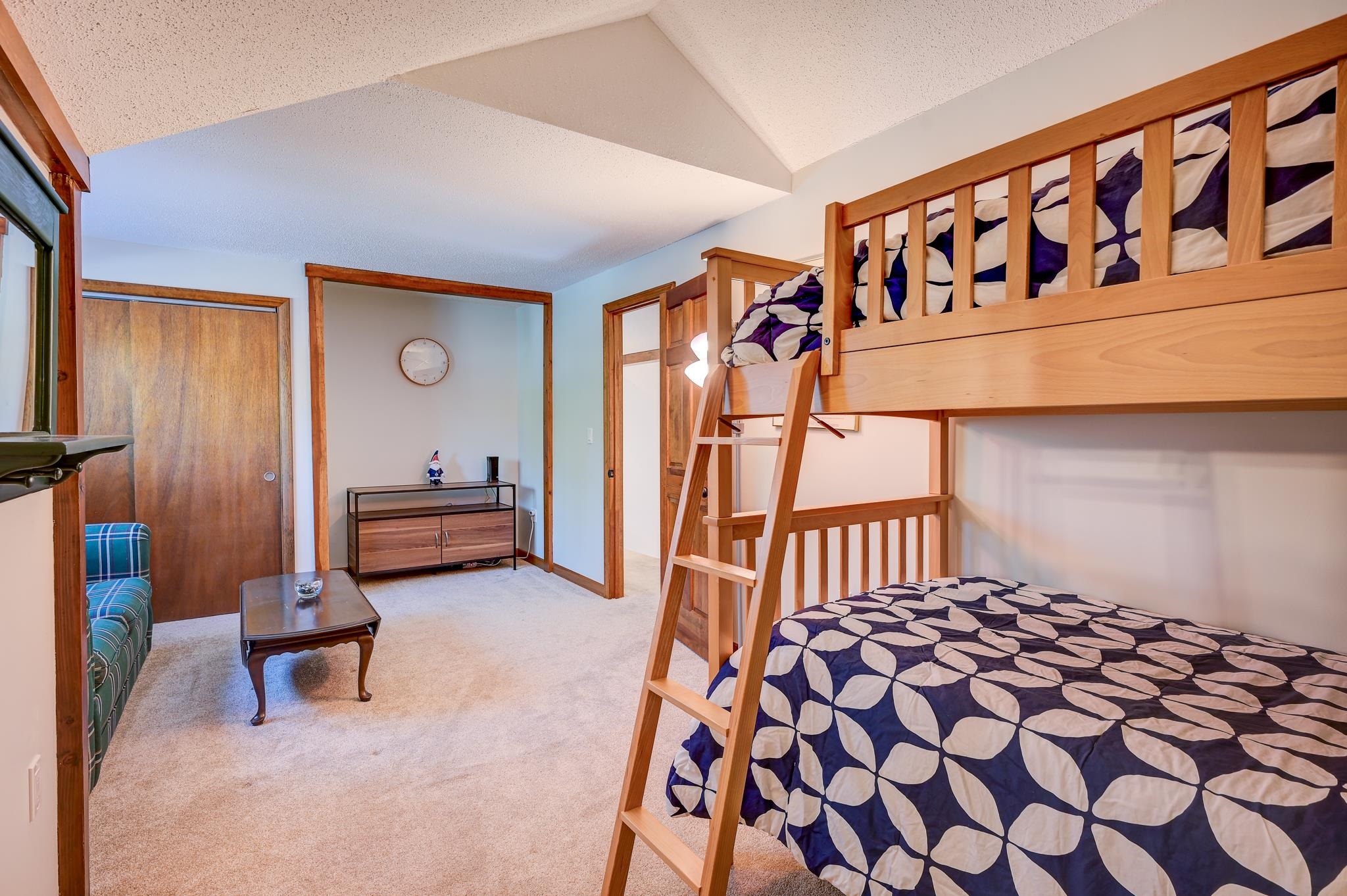 Bedroom with a wooden bunk bed, patterned navy-and-white bedding, and a plaid loveseat.