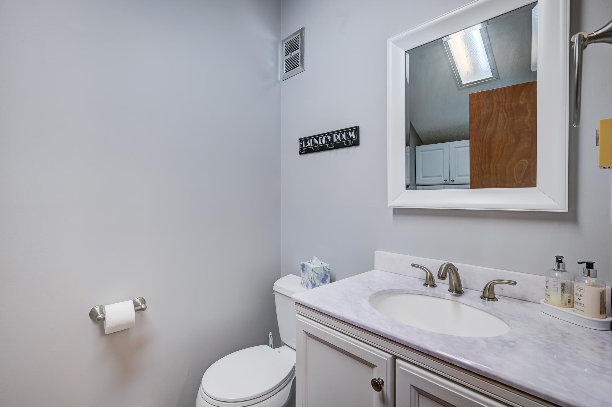 Bathroom vanity with a marble-look counter, oval sink, and mirror reflecting white cabinets and a wood door.