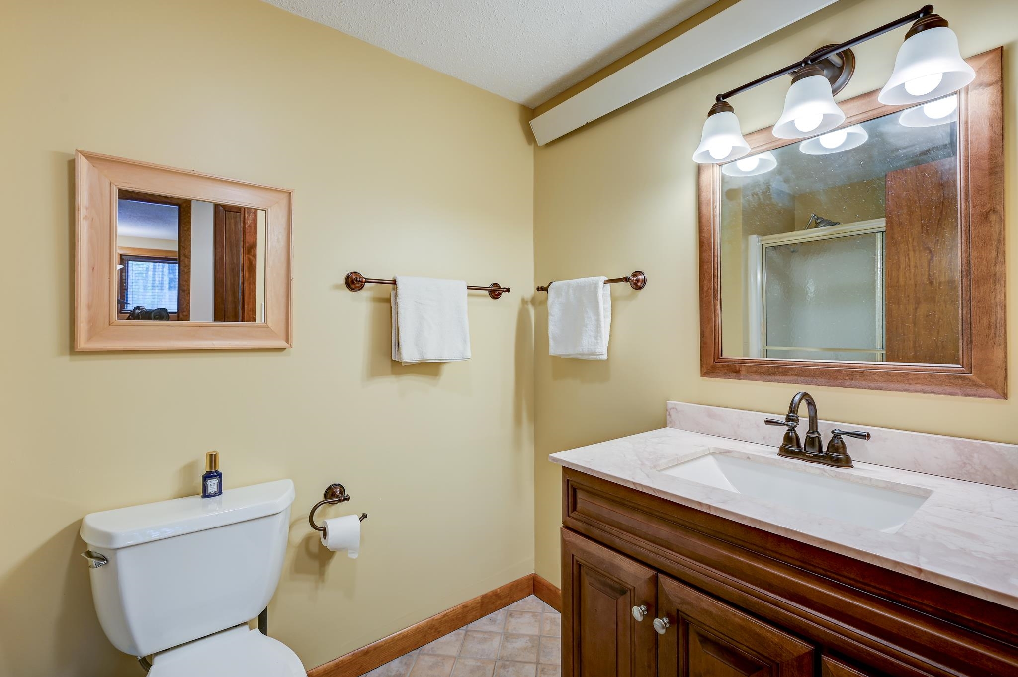Bathroom with a marble vanity, dark wood cabinetry, large framed mirror, and white toilet.