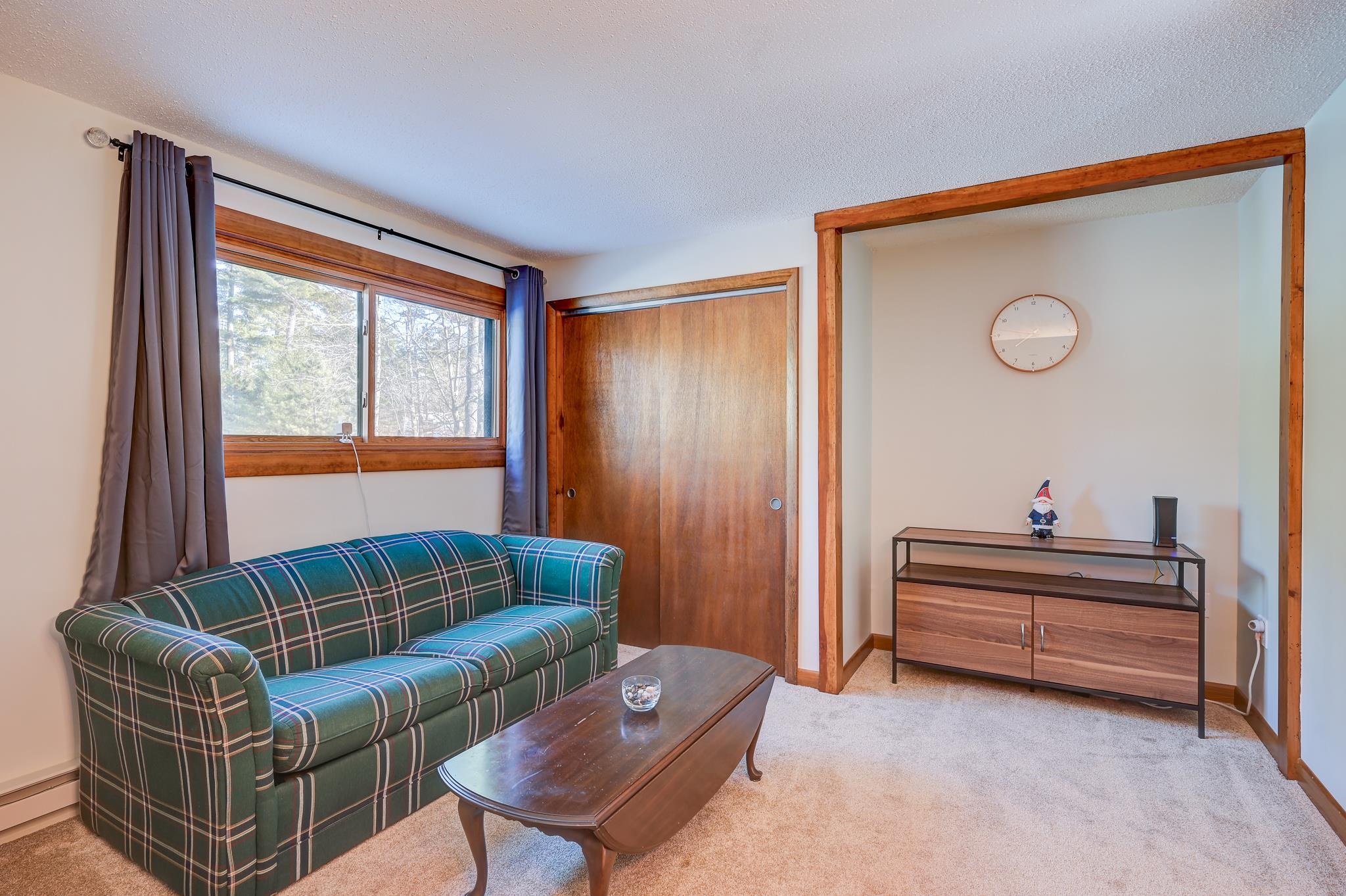 Living room with a green plaid sofa, wood-trimmed window, and wooden coffee table.