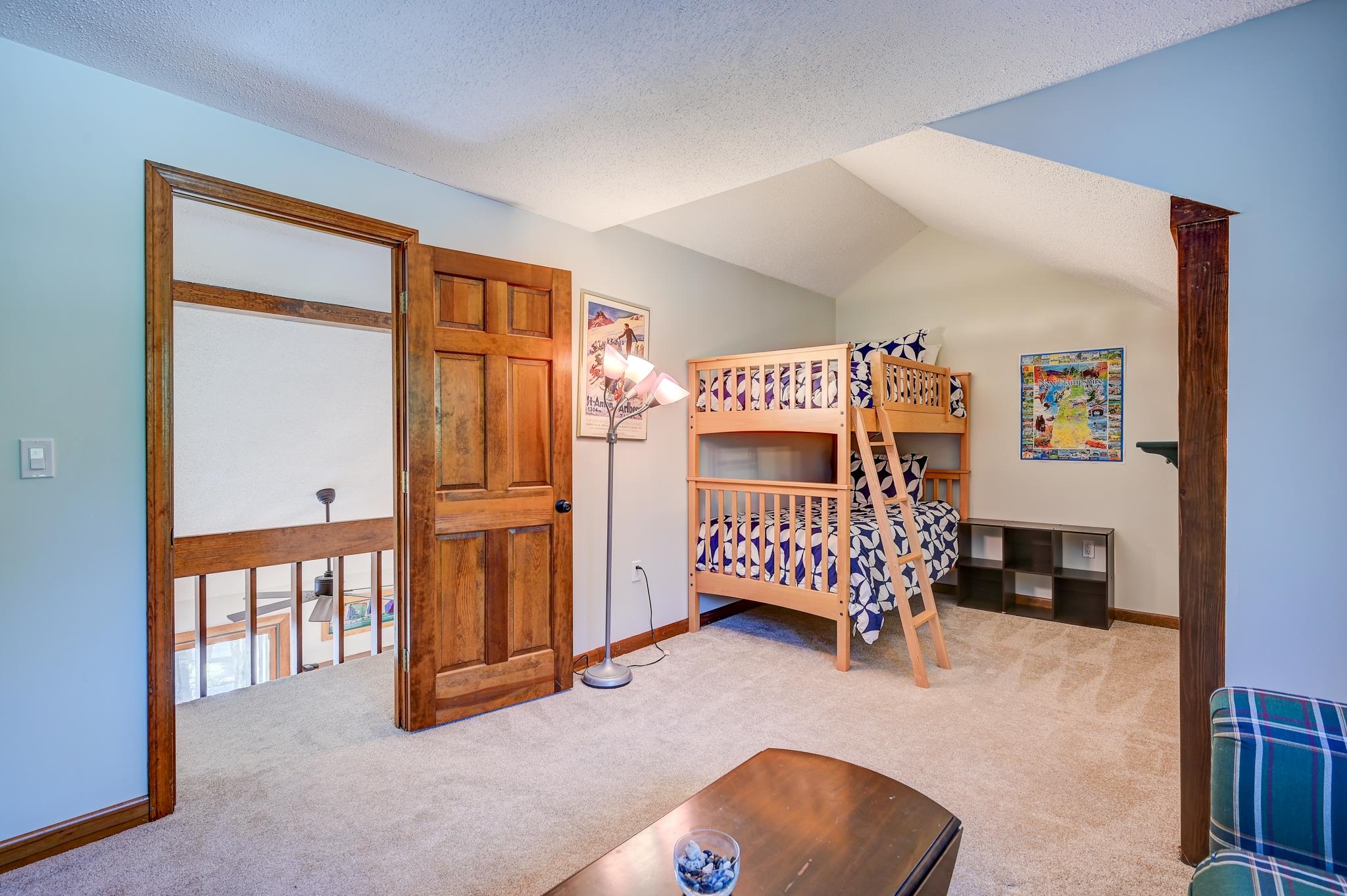 Loft bedroom with a wooden bunk bed, patterned bedding, and a vaulted ceiling.