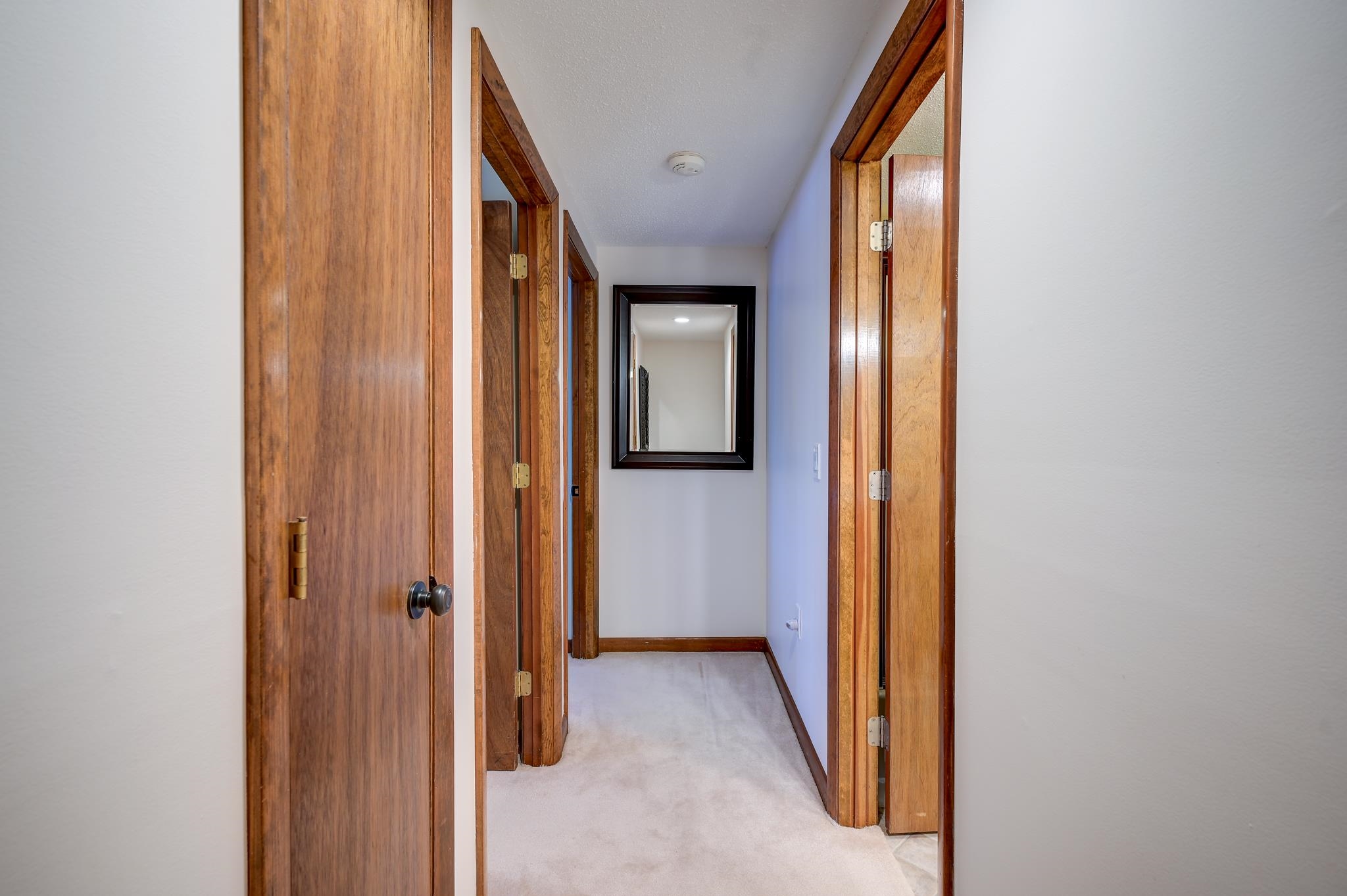 Carpeted hallway with open wood doors and a dark-framed mirror at the far end.