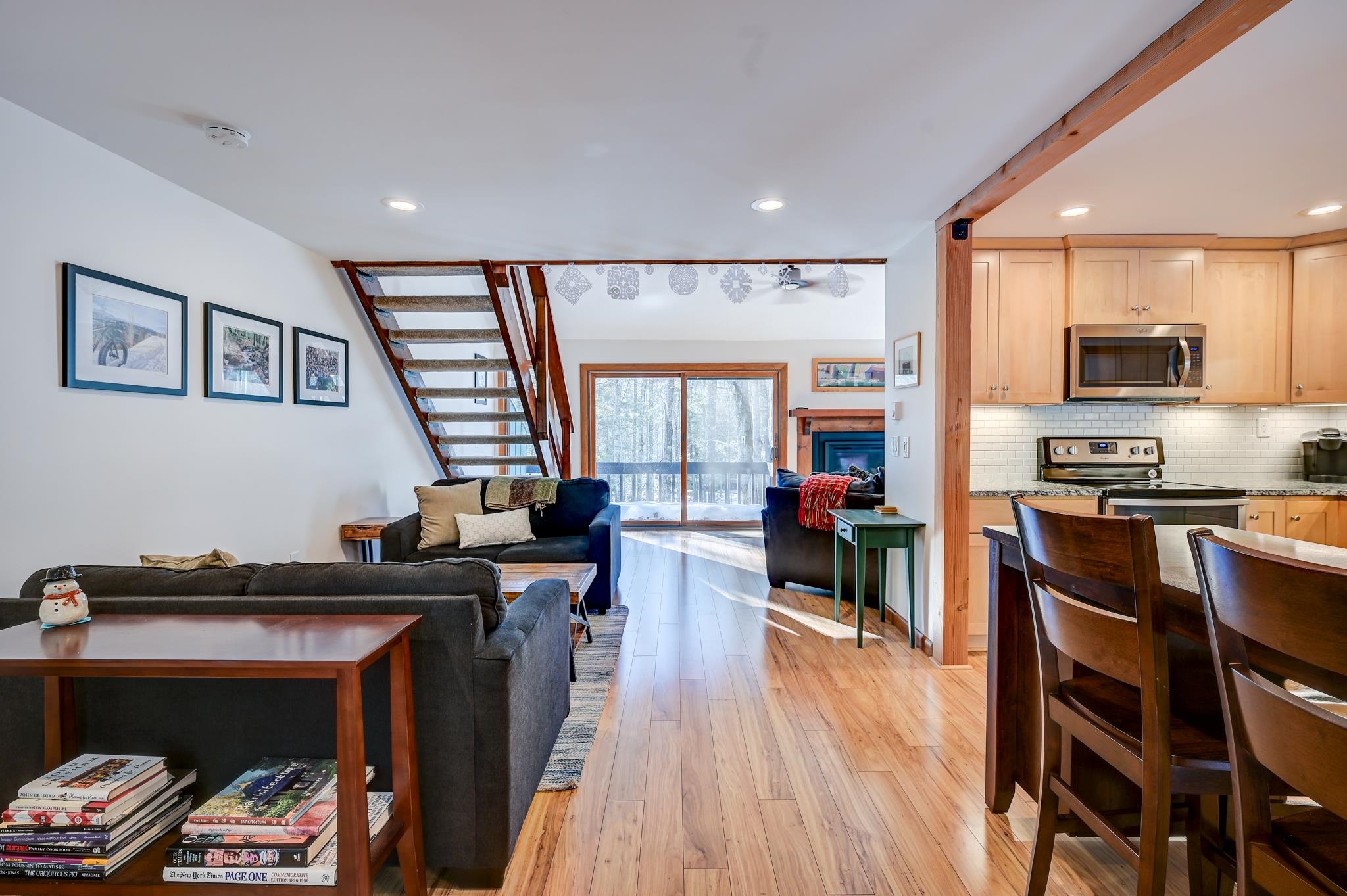 Open-plan living room and kitchen with wood floors, an open staircase, and snowy woods beyond the sliding doors.