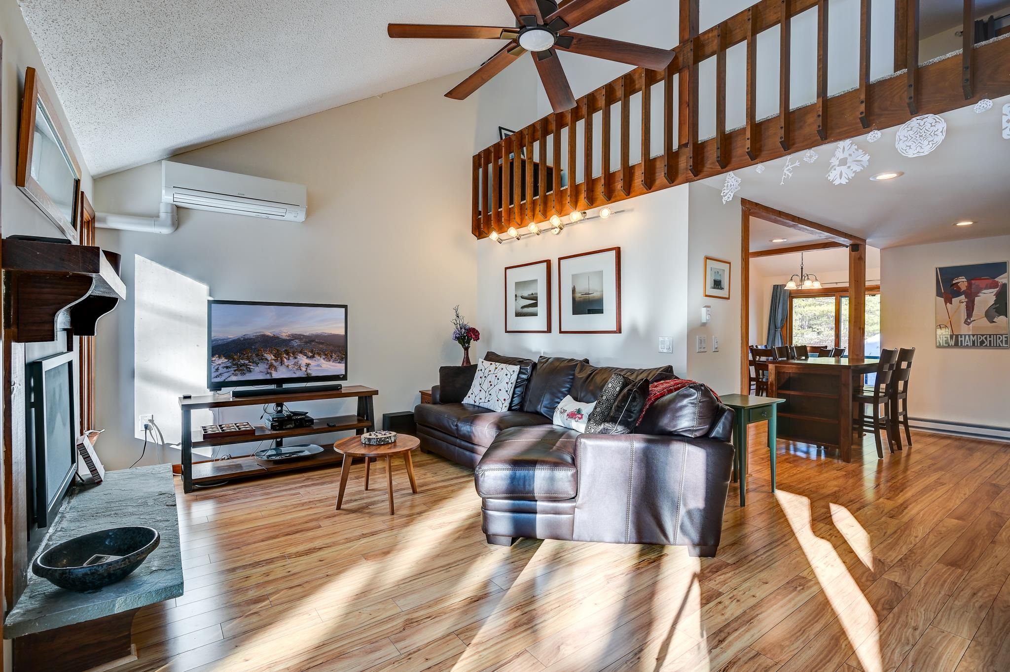 Open-plan living room with leather sectional, fireplace, wood floors, and a loft railing above.