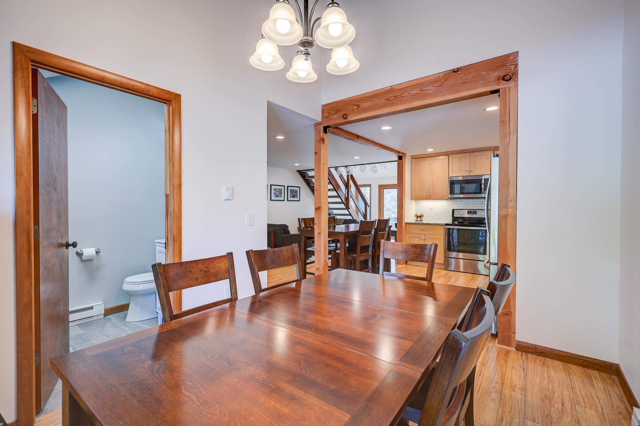 Dining area with a large wood table, exposed beams, and an open kitchen beyond.