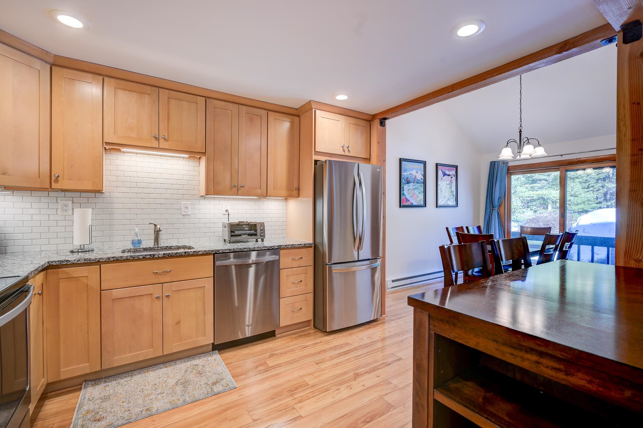 Kitchen with wood cabinetry and stainless steel appliances opens to a dining area beside sliding glass doors.