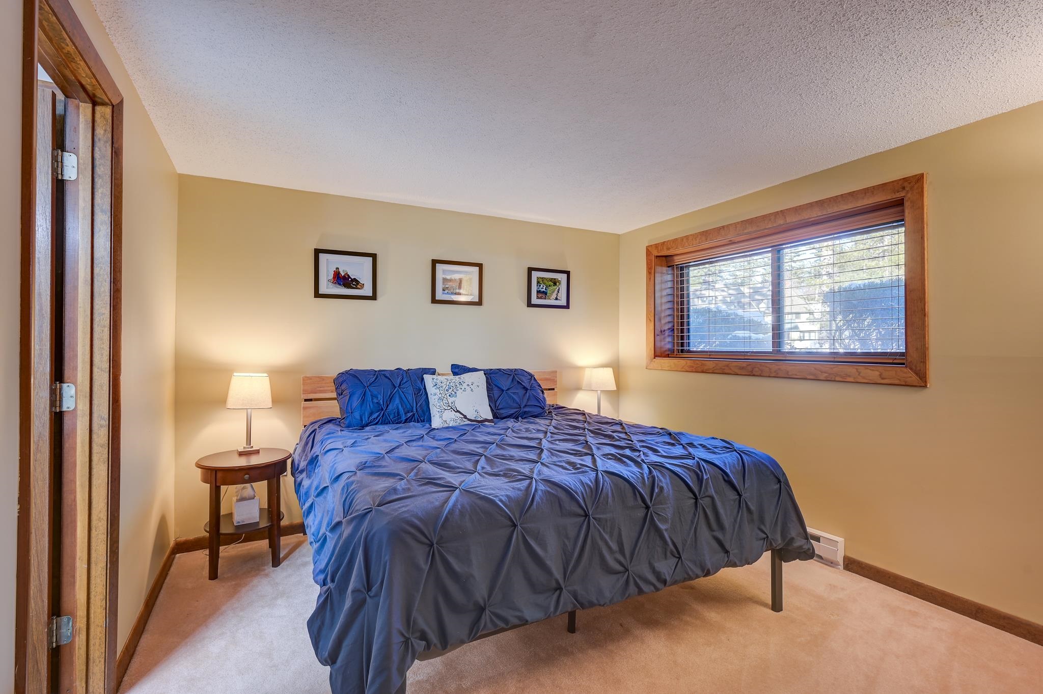 Bedroom with blue and gray bedding, bedside lamps, and a wood-trimmed window.