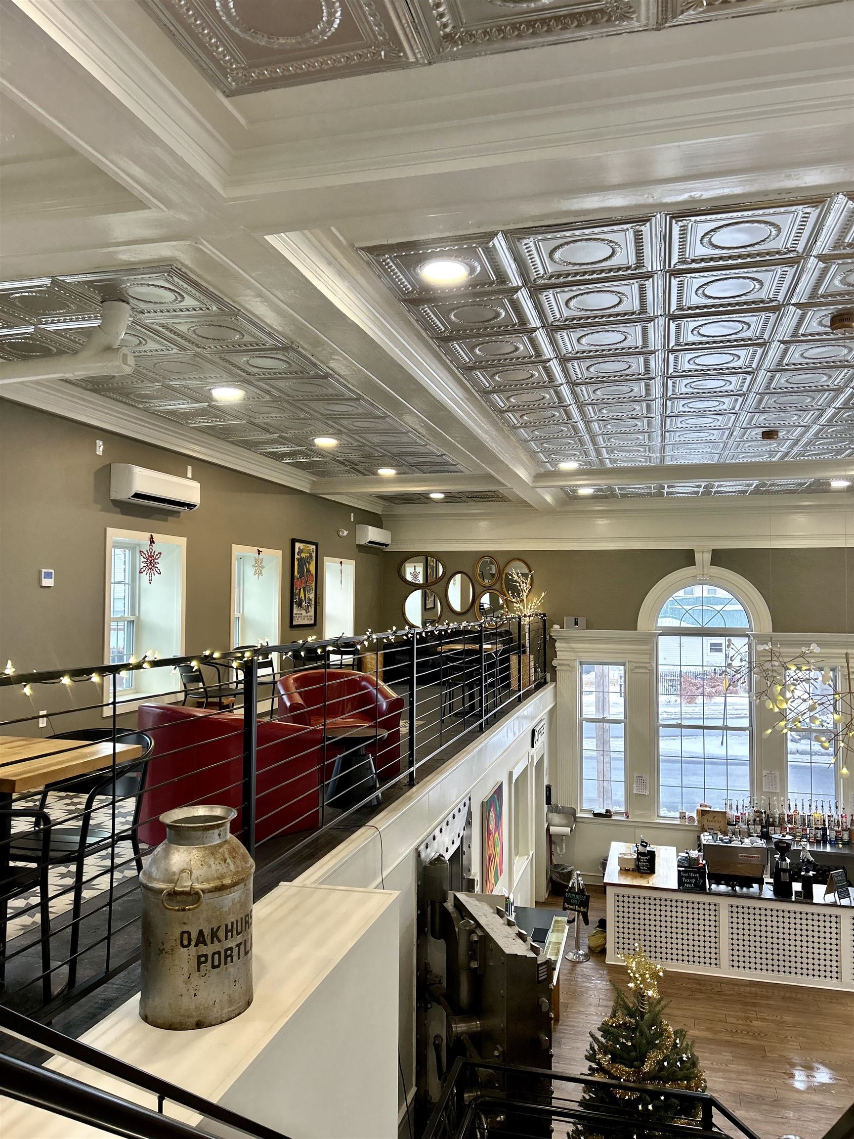 Commercial interior with an ornate metal-tile ceiling, red seating, a bar counter, and large arched windows.