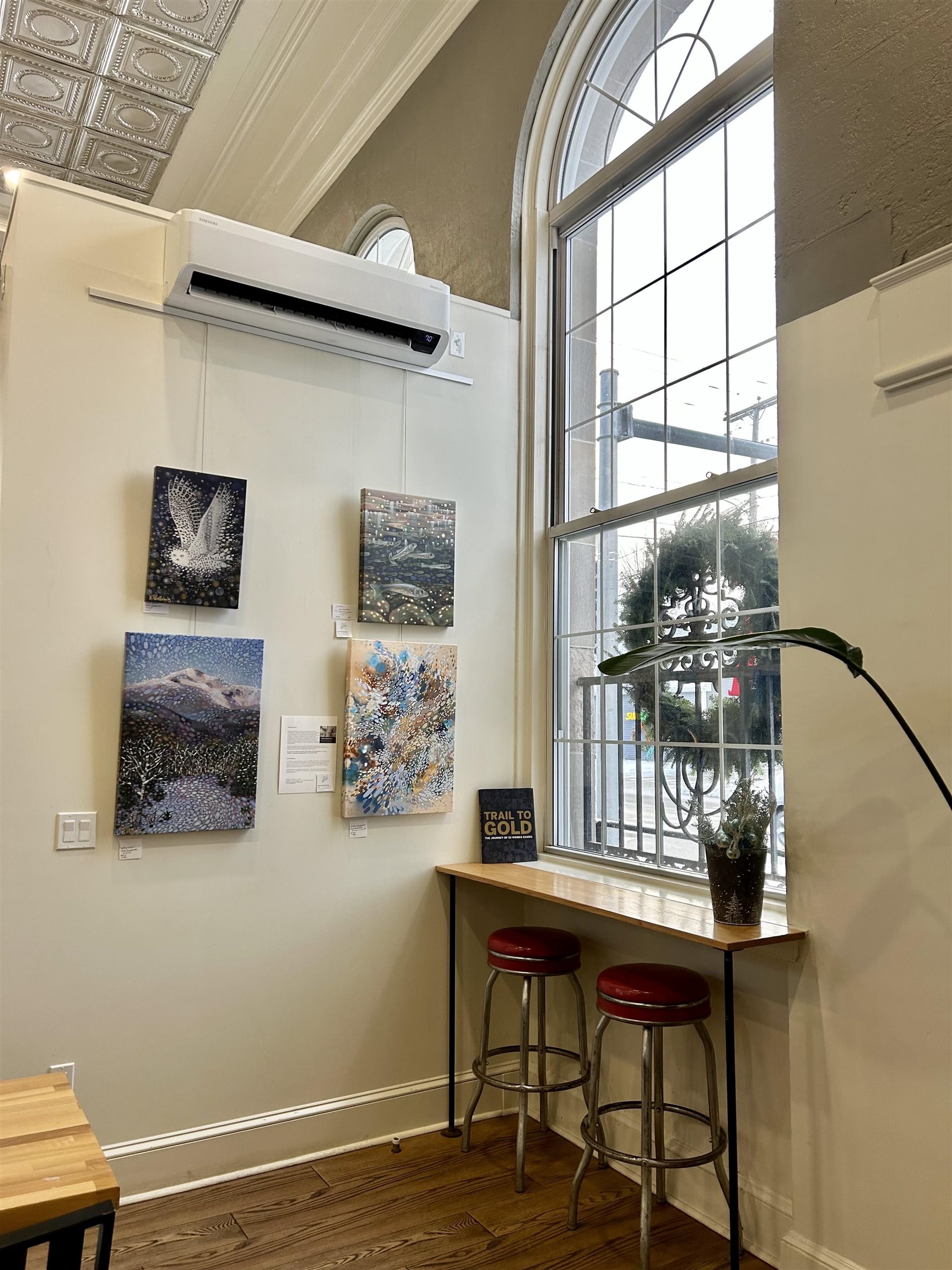 Interior with a tall arched window, wall art, and a counter with two stools.