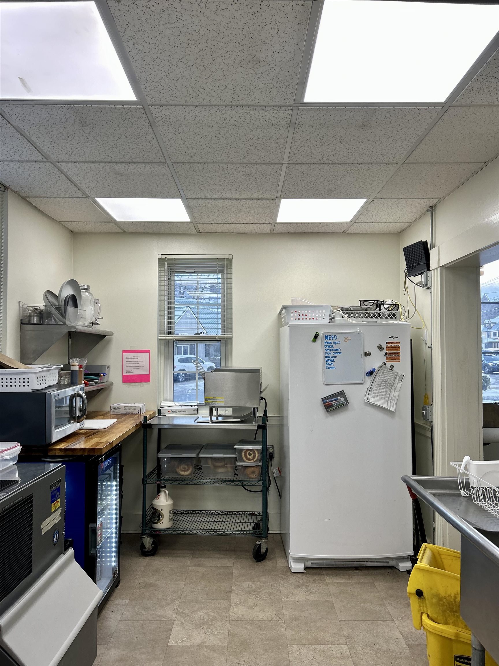 Commercial kitchen with a large white refrigerator, stainless prep surfaces, and a rolling storage rack.