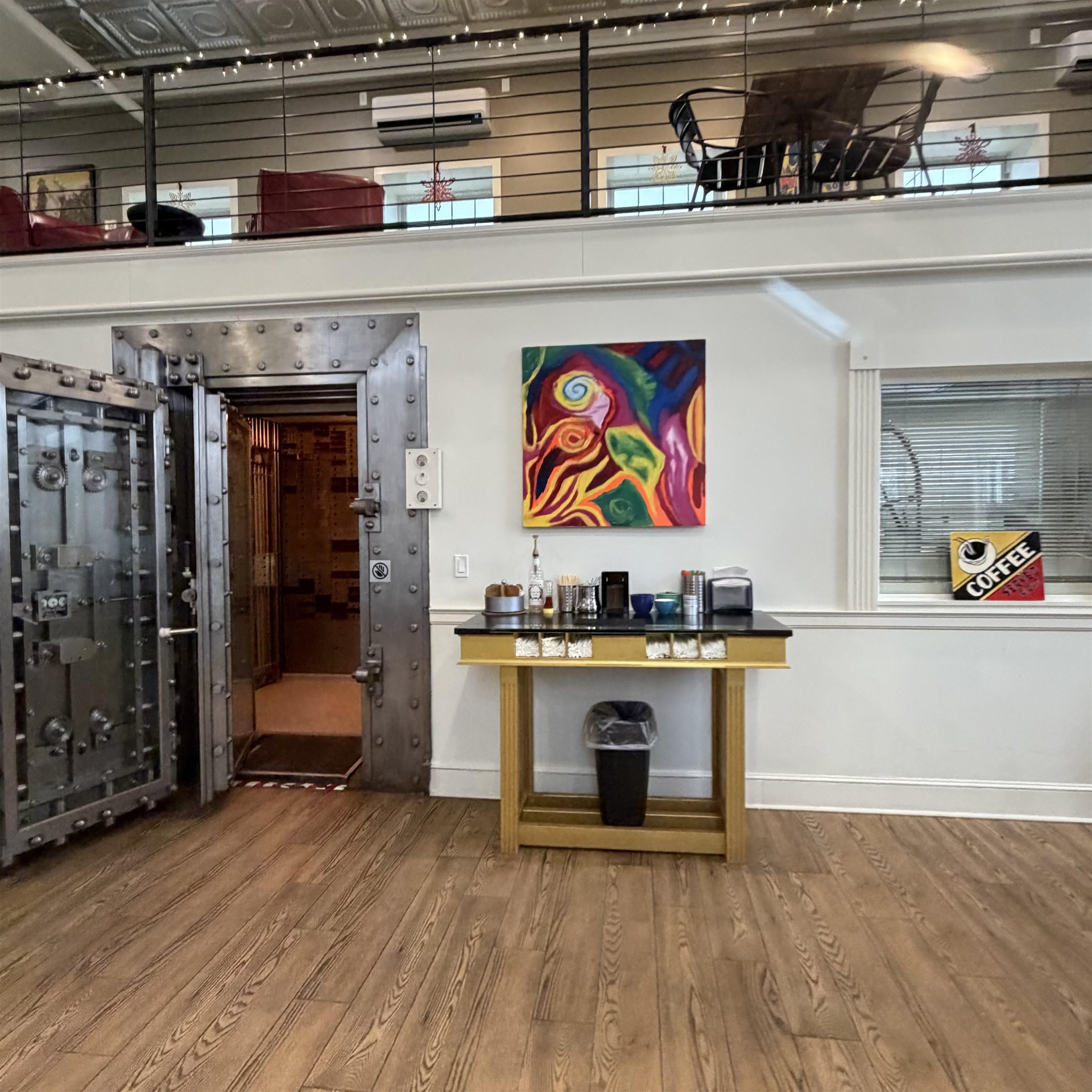 Commercial interior with an open steel vault, coffee station, and furnished mezzanine.