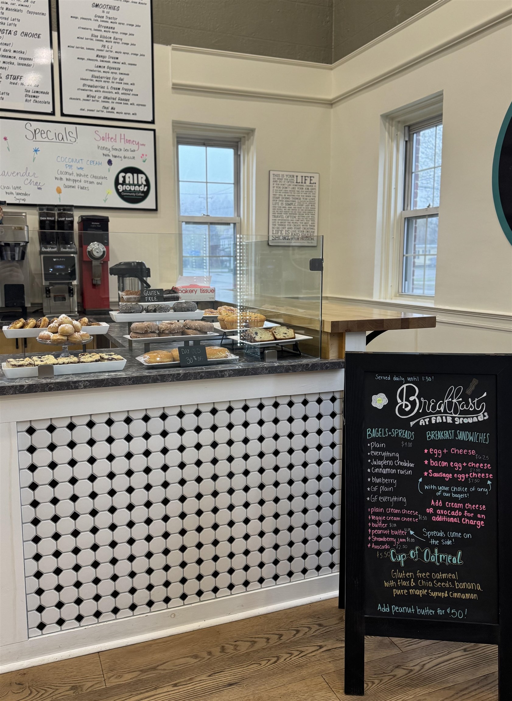 Café counter with pastries in a glass display, coffee equipment, and a breakfast chalkboard.