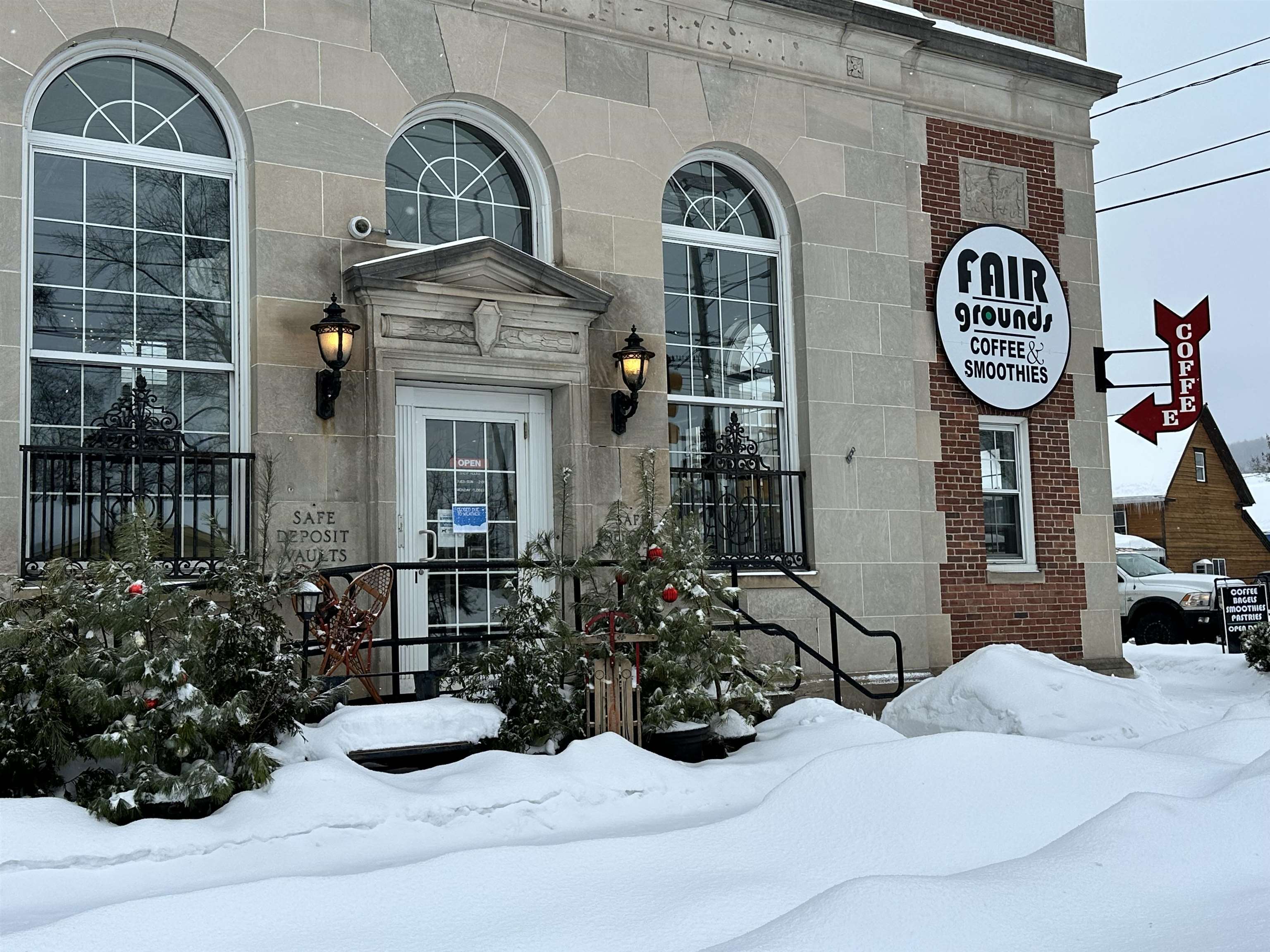 Stone-front commercial building with arched windows and Fair Grounds coffee signage, surrounded by deep snow.