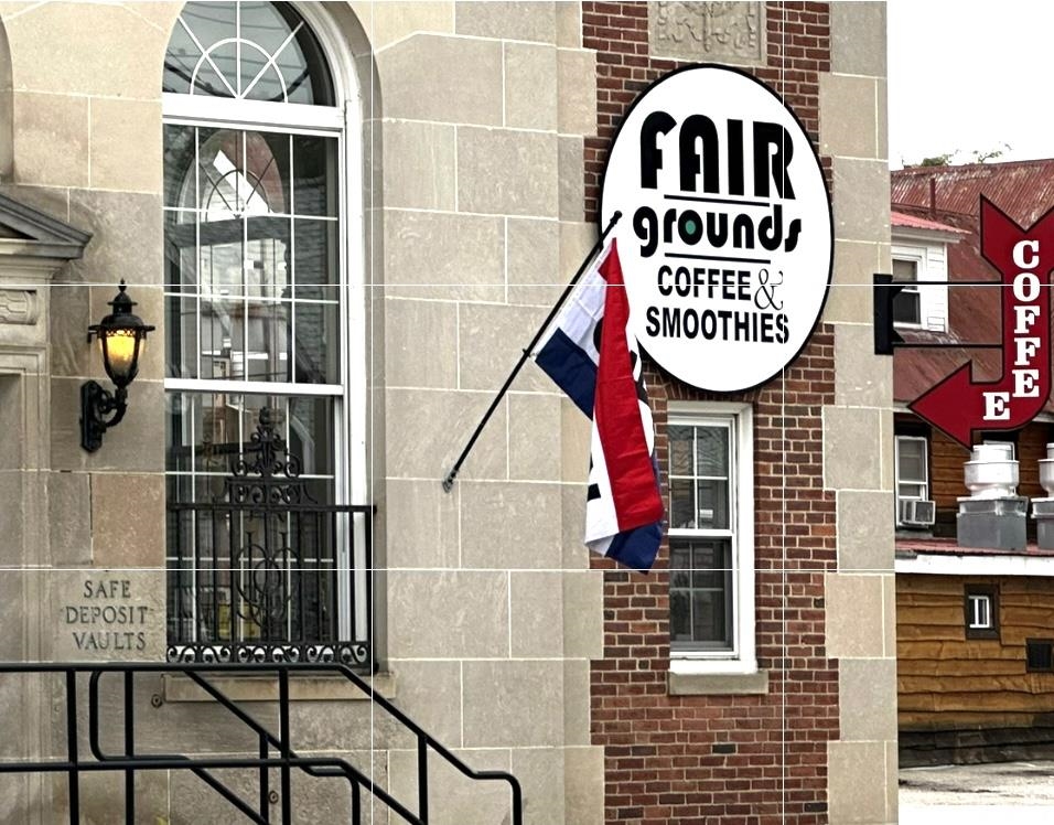 Stone-and-brick storefront with a Fair Grounds coffee sign, arched window, and exterior stairs.