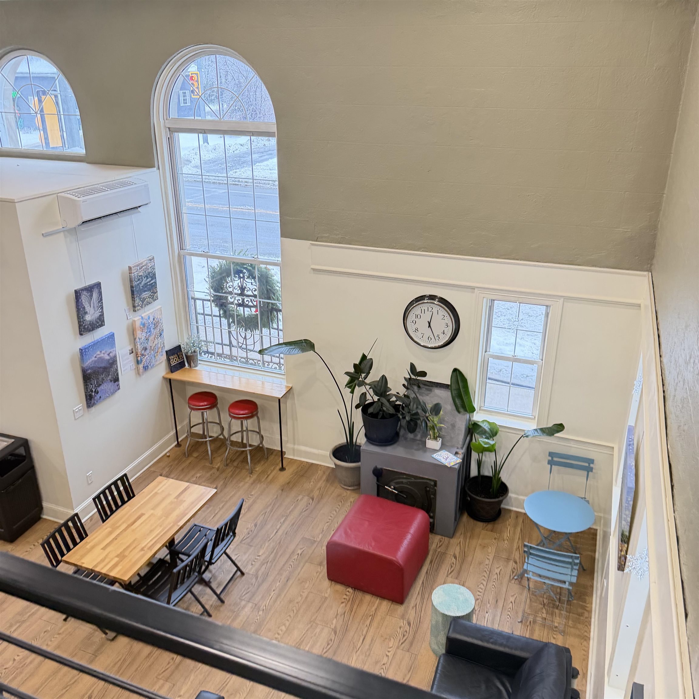 Furnished double-height living and dining area with hardwood floors, arched windows, and colorful seating.
