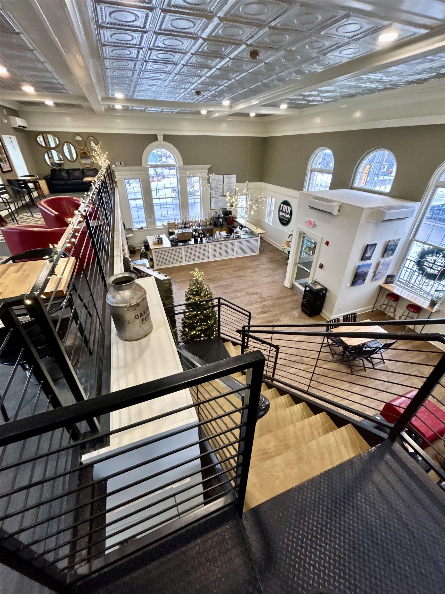 Furnished commercial interior with café counter, arched windows, ornate tin ceiling, and black metal staircase railings.