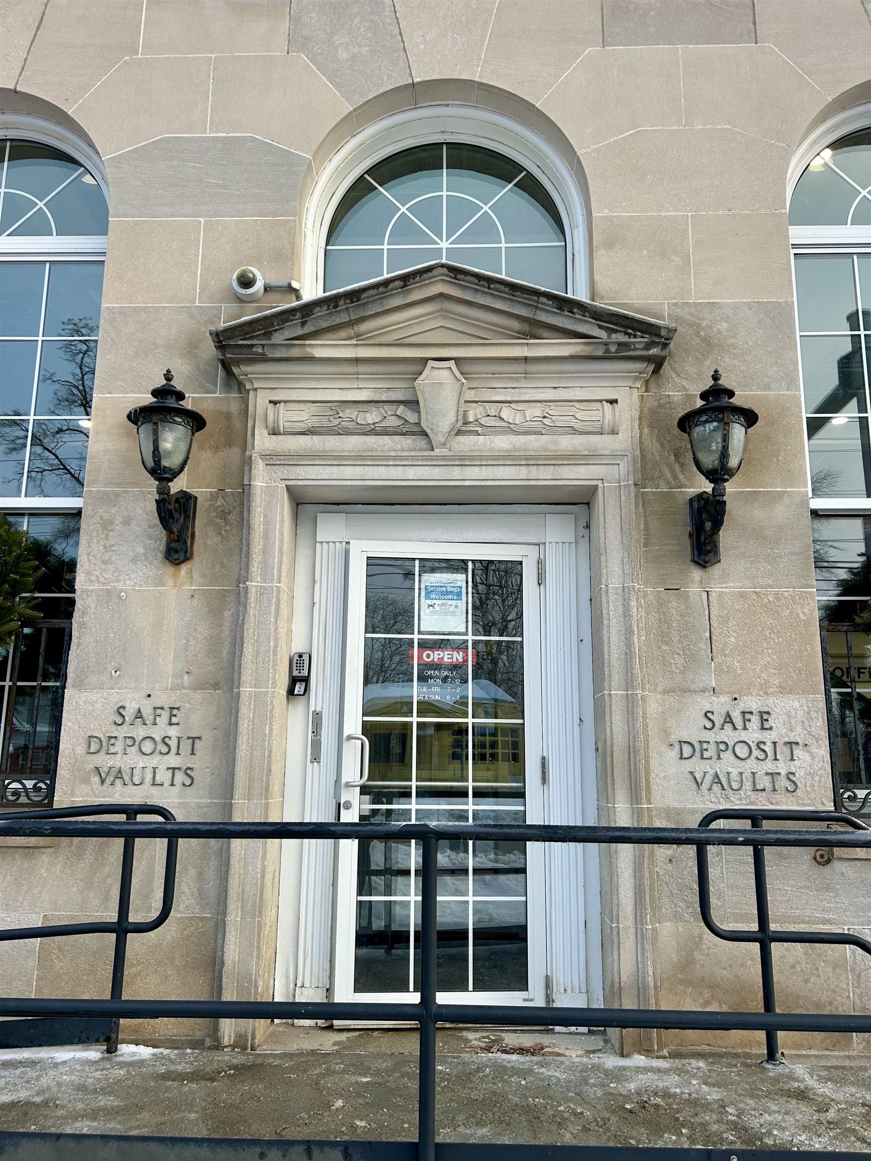 Stone building entrance with an ornate pediment, arched windows, and “SAFE DEPOSIT VAULTS” lettering.
