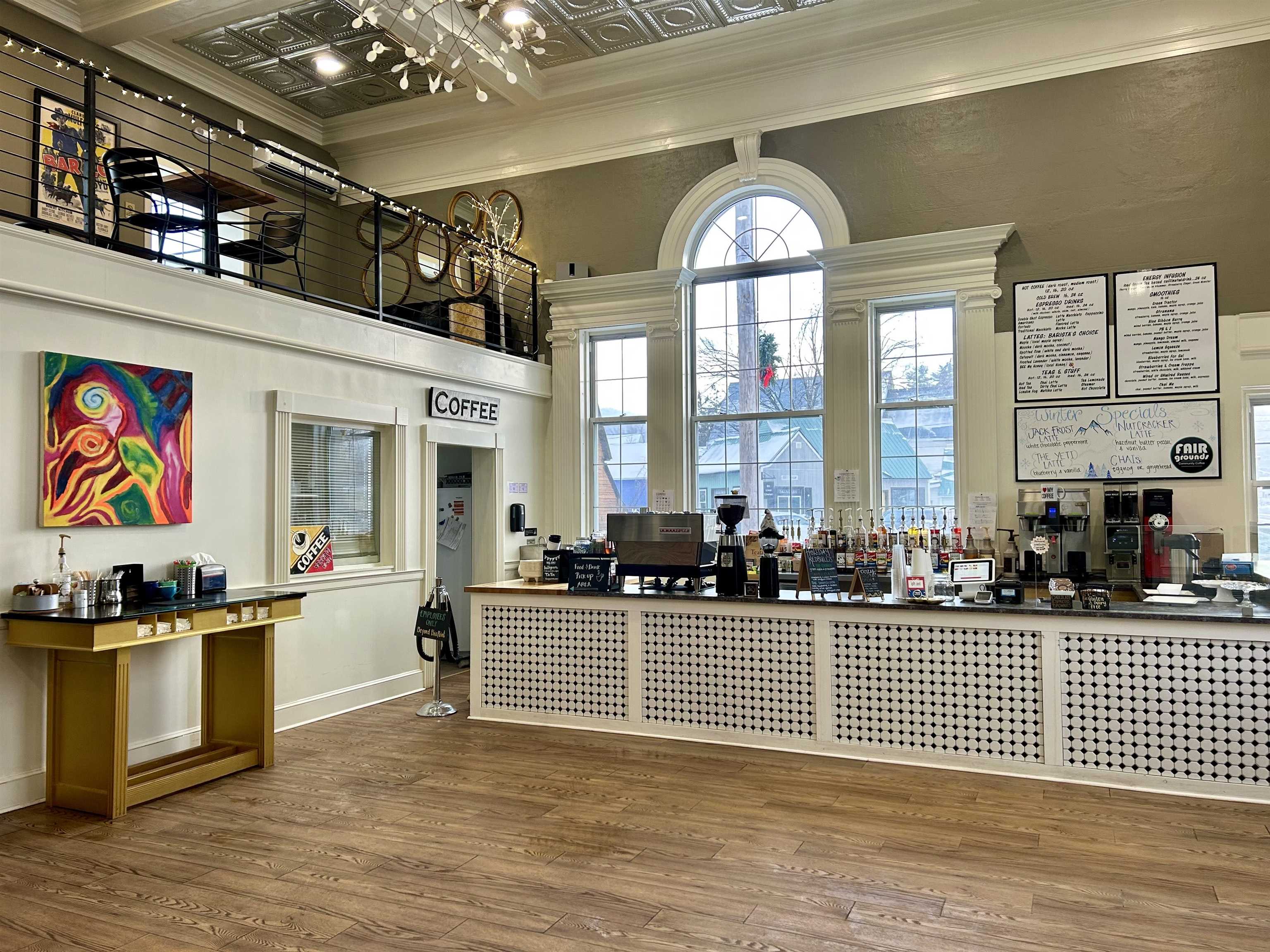 Coffee shop interior with a tiled service counter, tall arched windows, and a mezzanine.