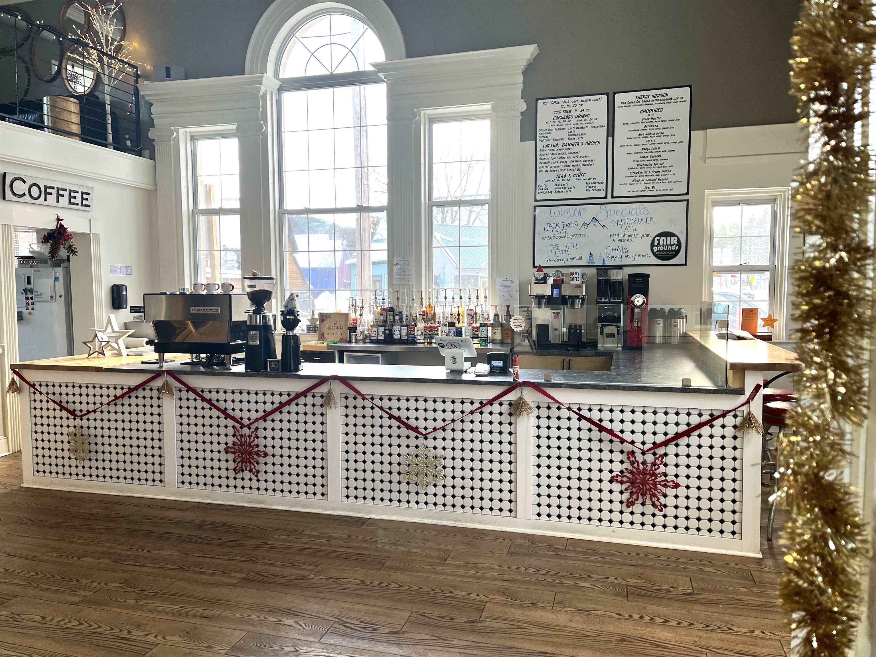 Coffee shop counter with patterned tile, espresso machines, and tall arched windows.